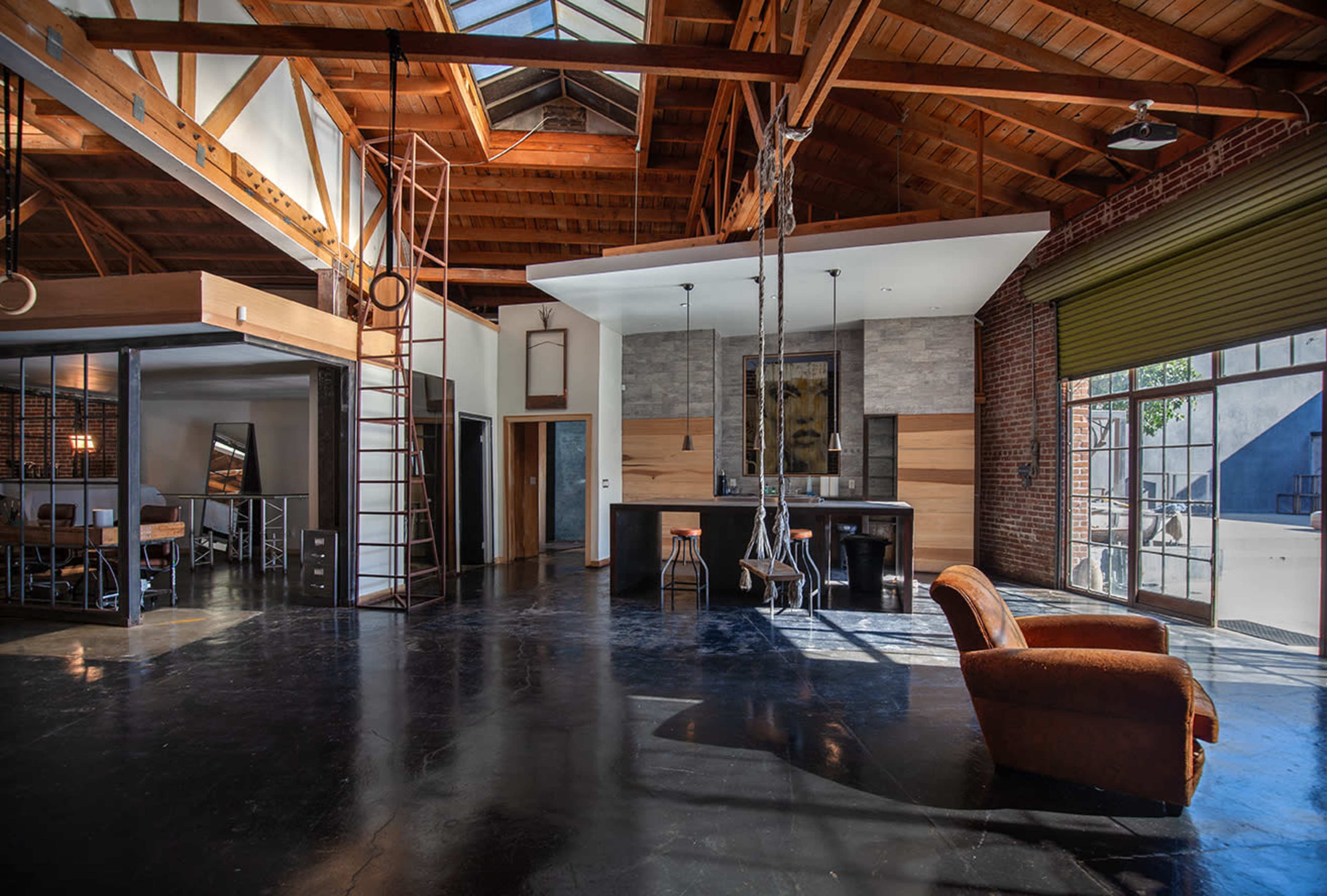 A spacious interior of a modern loft with high wooden ceilings, a kitchen area, and a seating area featuring an armchair.