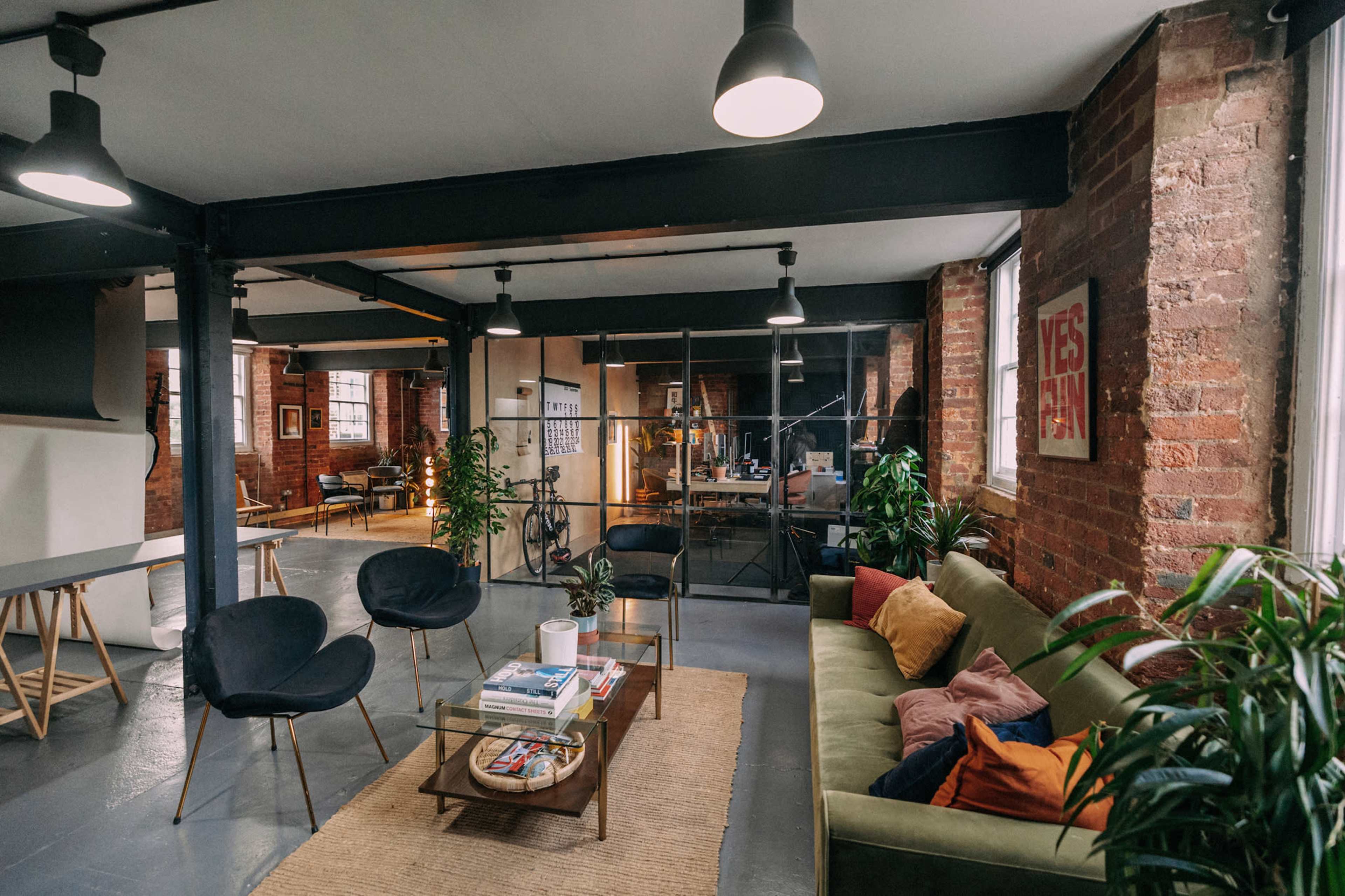 A stylish office space with exposed brick walls, modern furniture, and a cozy seating area surrounded by plants.