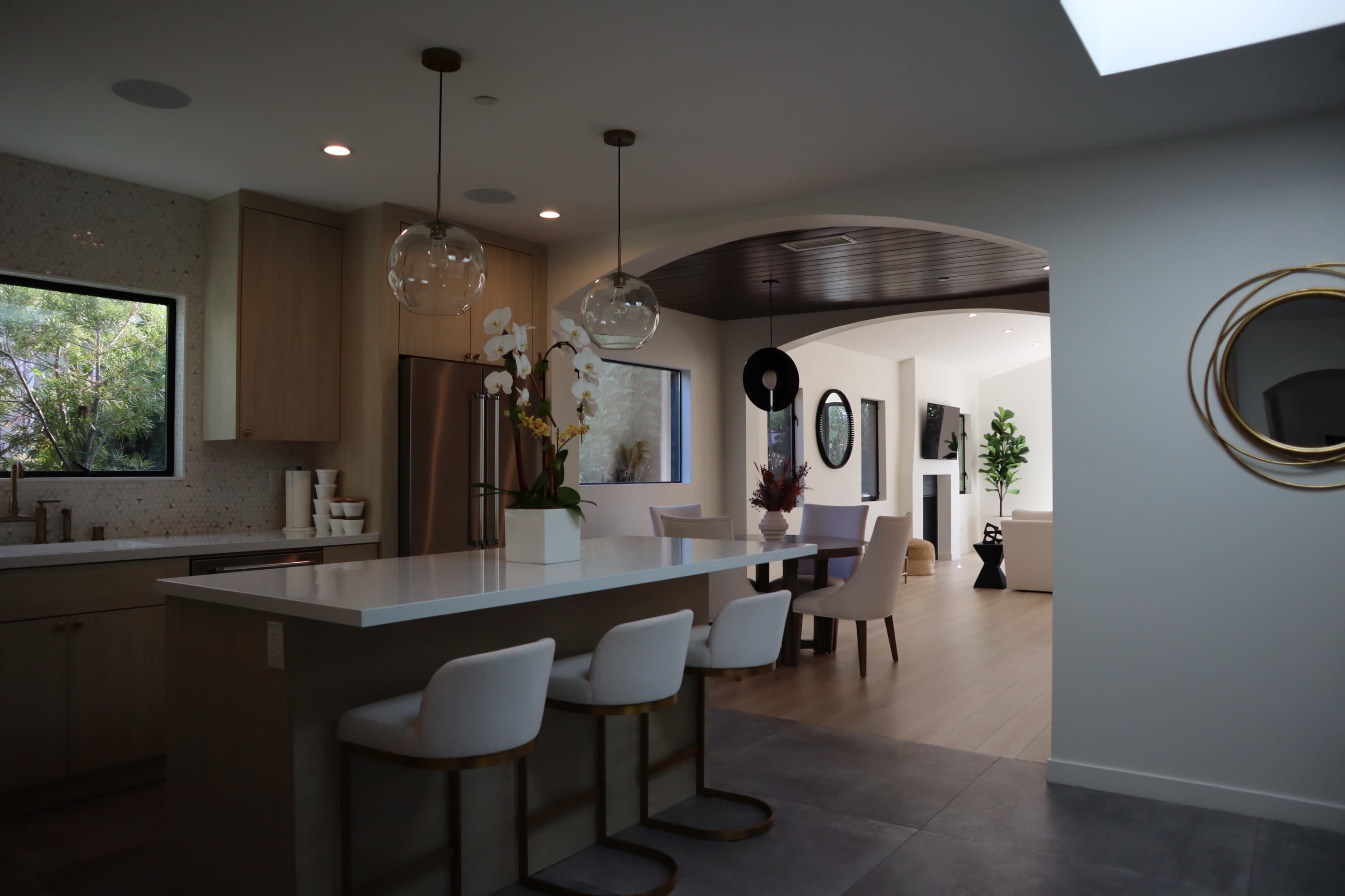 A modern kitchen with a central island and three chairs, adjacent to a dining area with a round table and a living room visible in the background.