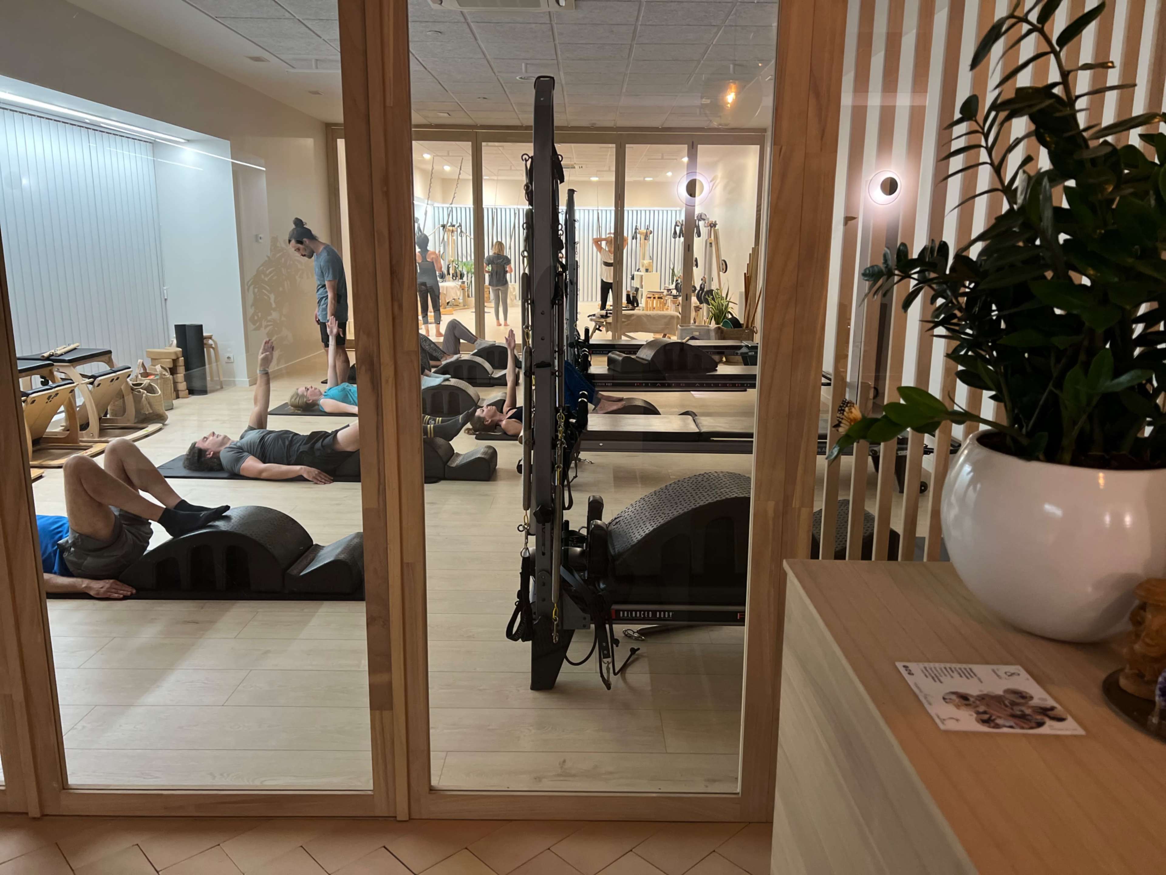 A fitness studio through a glass wall, where several people are lying on exercise mats, while others are participating in a workout session.