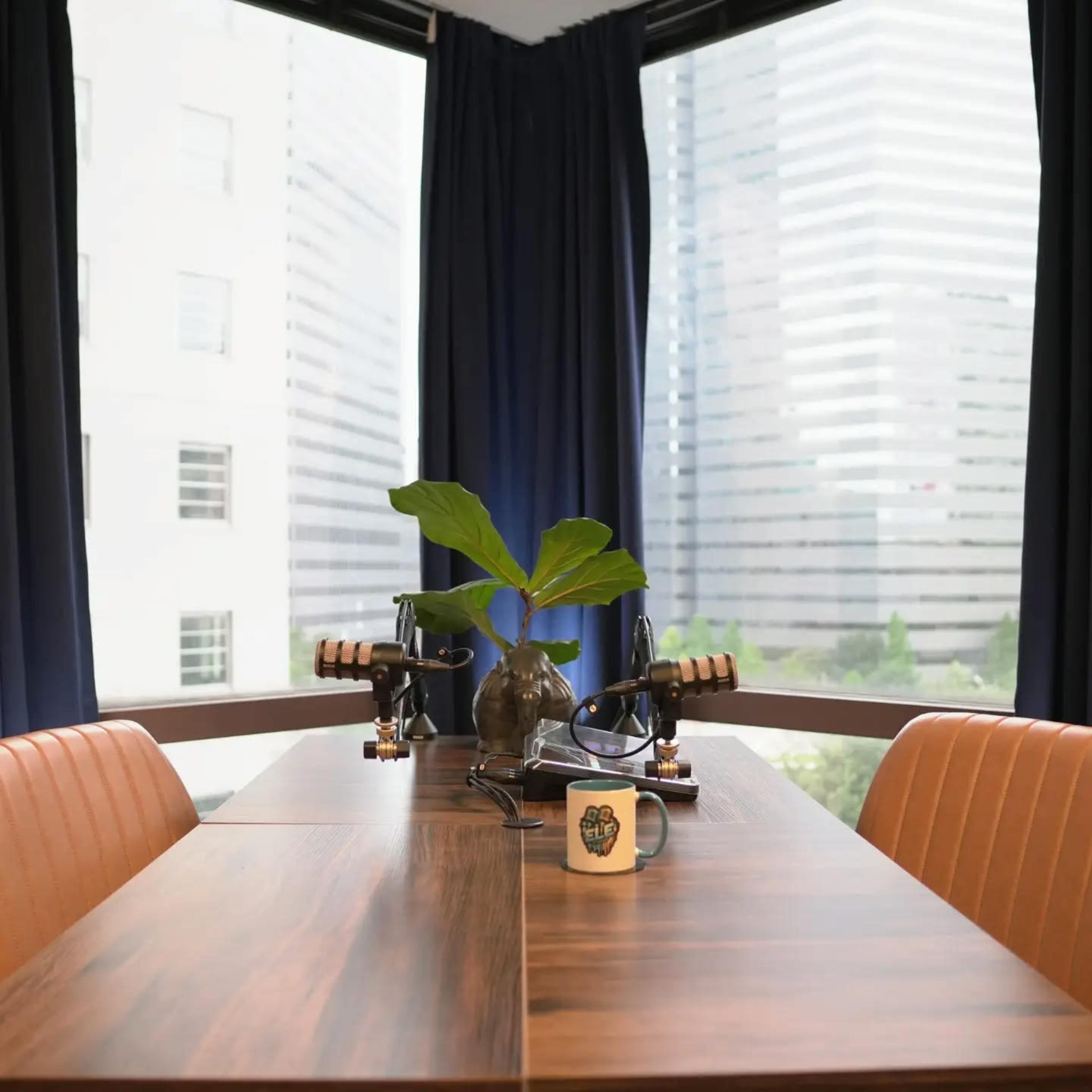 A wooden conference table with two ergonomic chairs is positioned by large windows, showcasing a view of nearby skyscrapers.