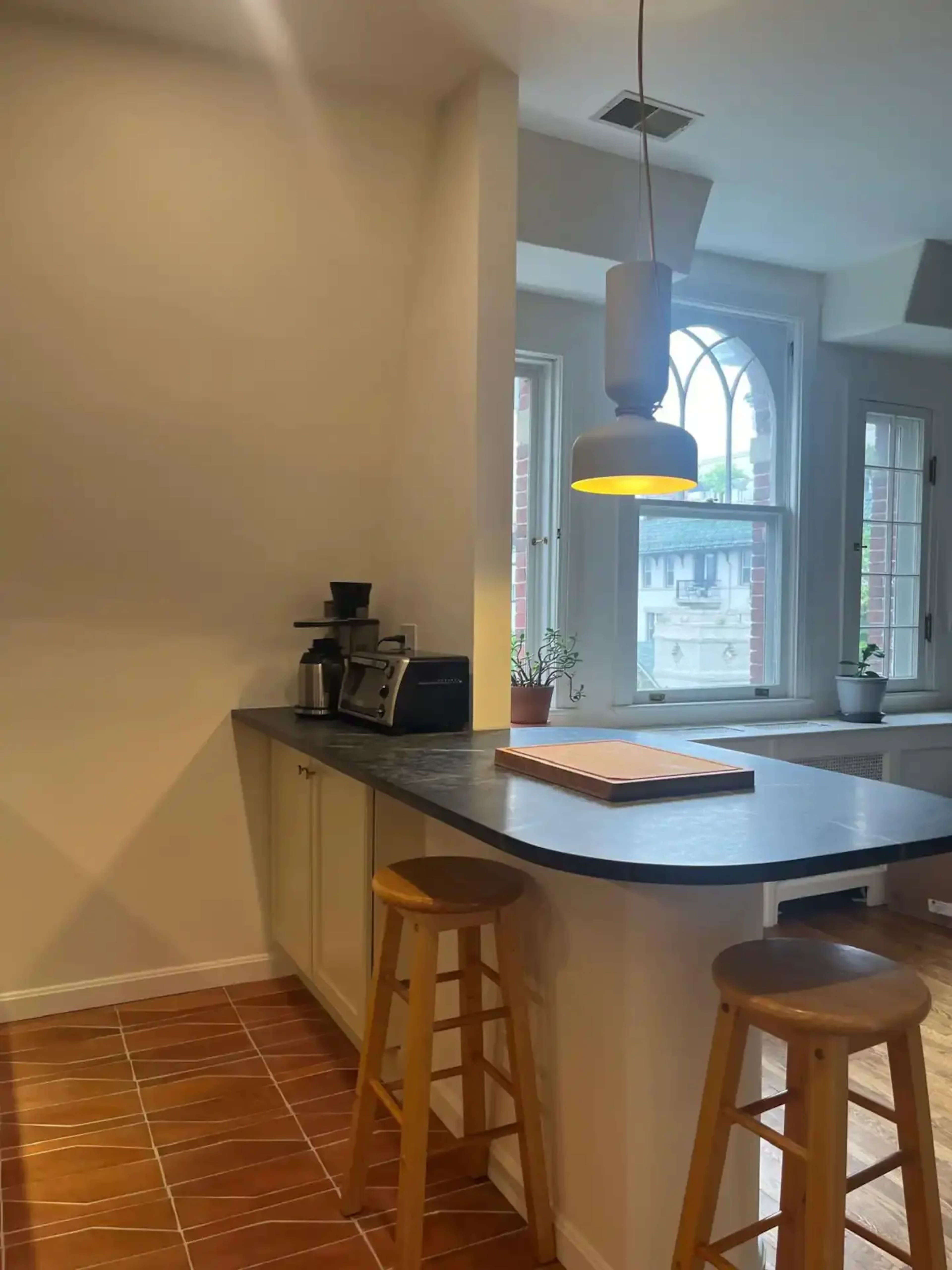 A modern kitchen features a countertop with bar stools, a coffee machine, and a pendant light illuminating the space.