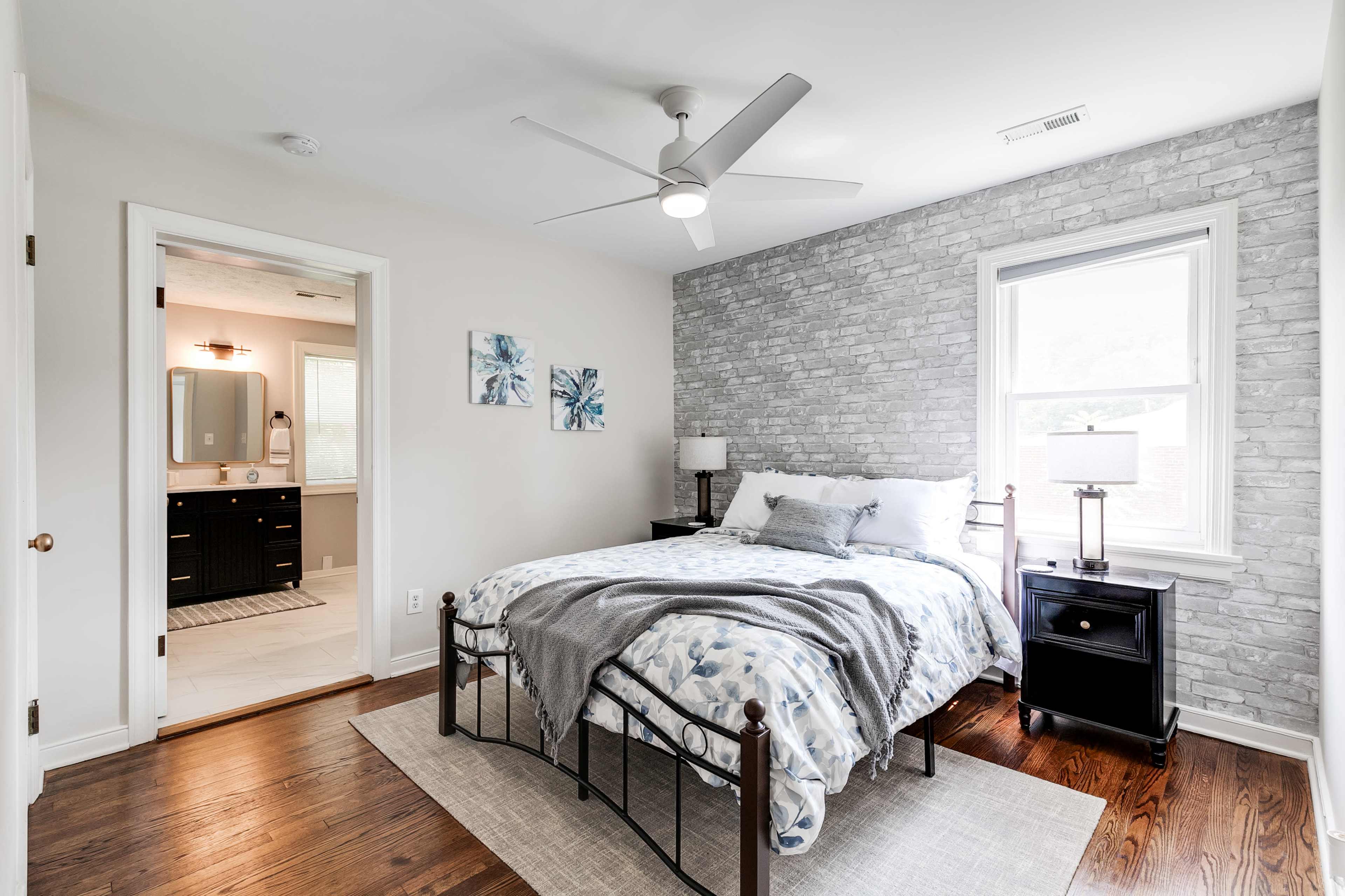 A well-lit bedroom featuring a metal bed frame with a patterned blanket, a nightstand, and a doorway leading to an adjoining bathroom.