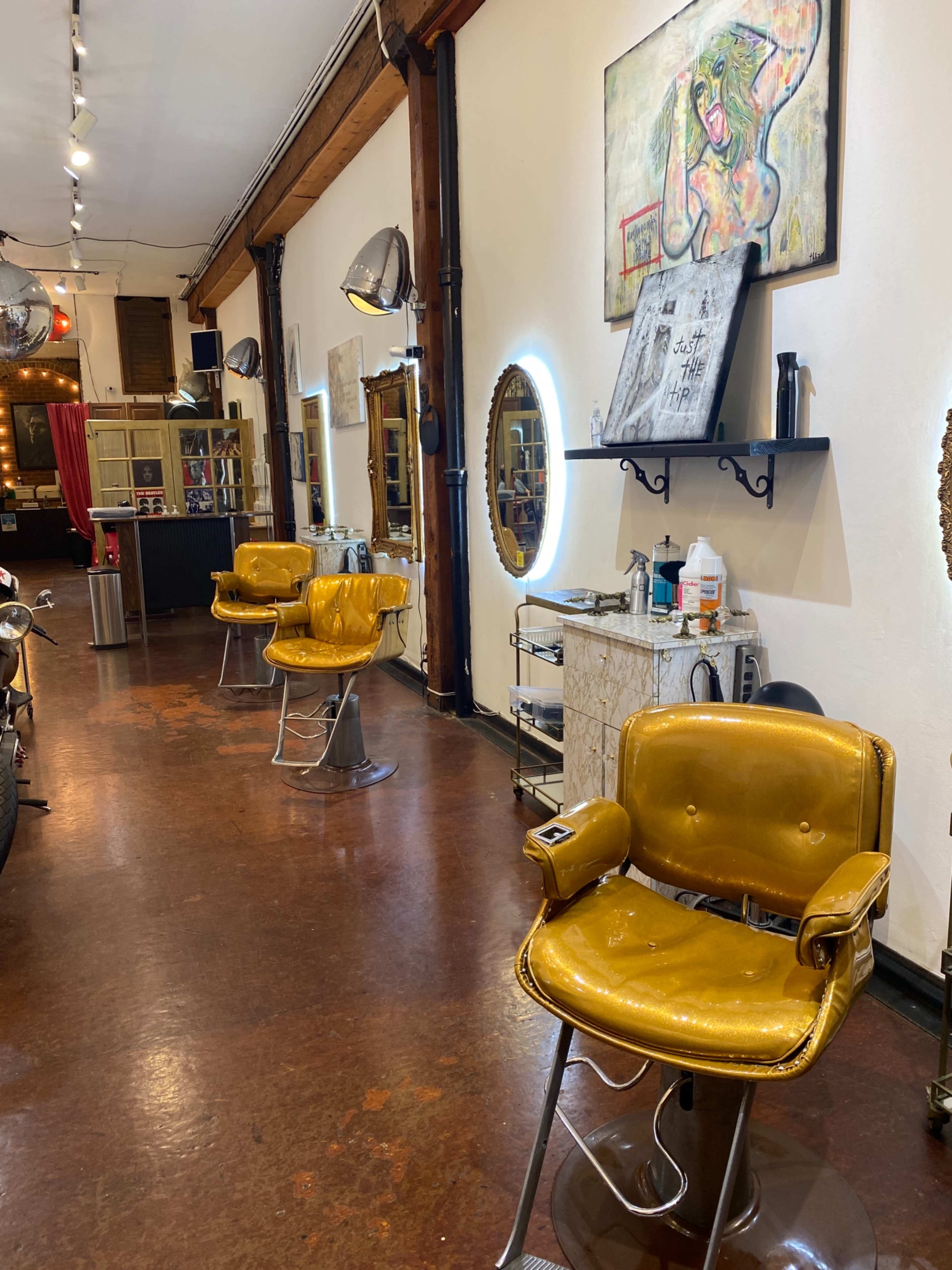 The image shows a hair salon with three vintage yellow chairs positioned in a row against a wall, with mirrors and various salon equipment in the background.