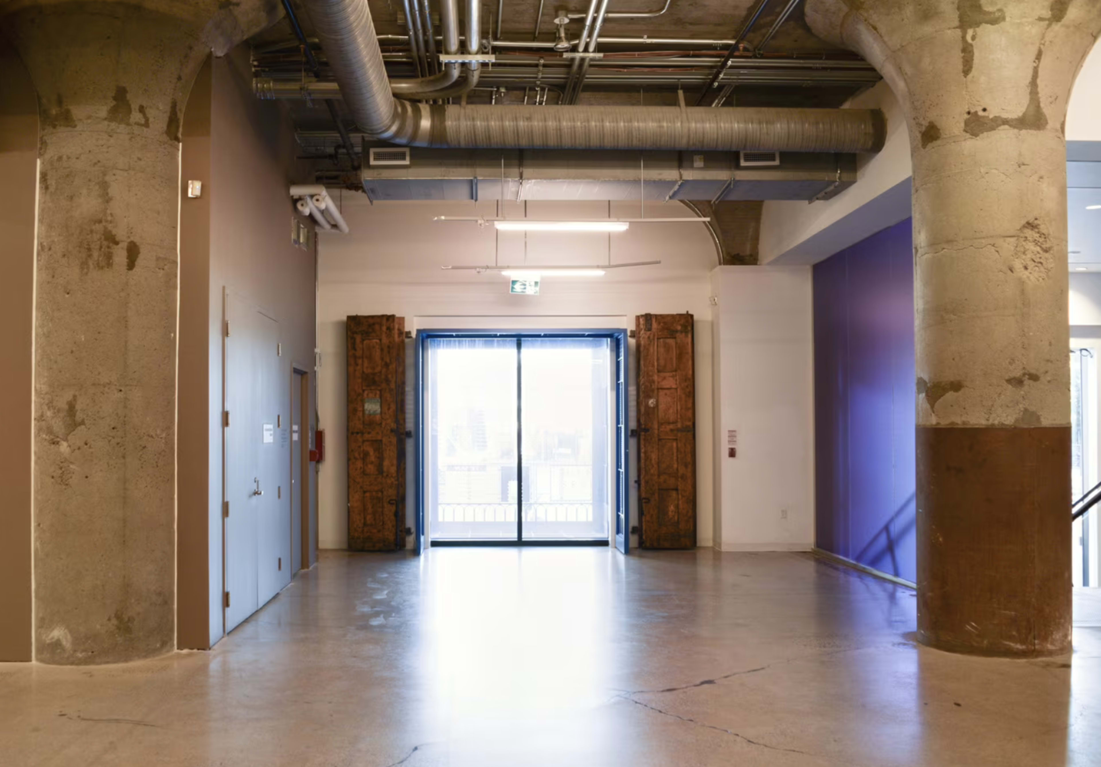 A hallway features concrete pillars and large double doors leading outside, with a purple wall on one side.