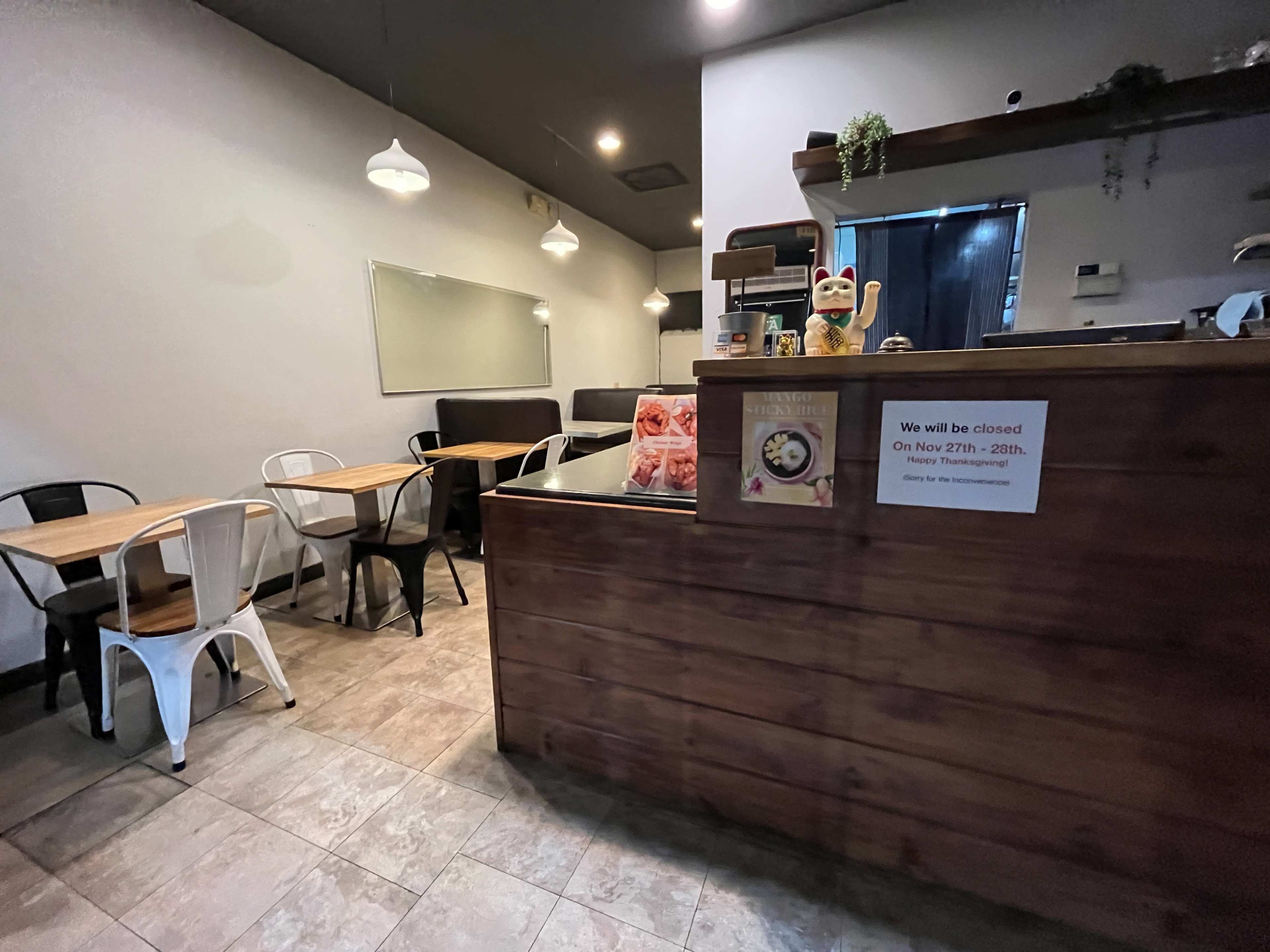 The image shows a small café interior with wooden counters, several tables, and a sign indicating the café will be closed on specific dates.