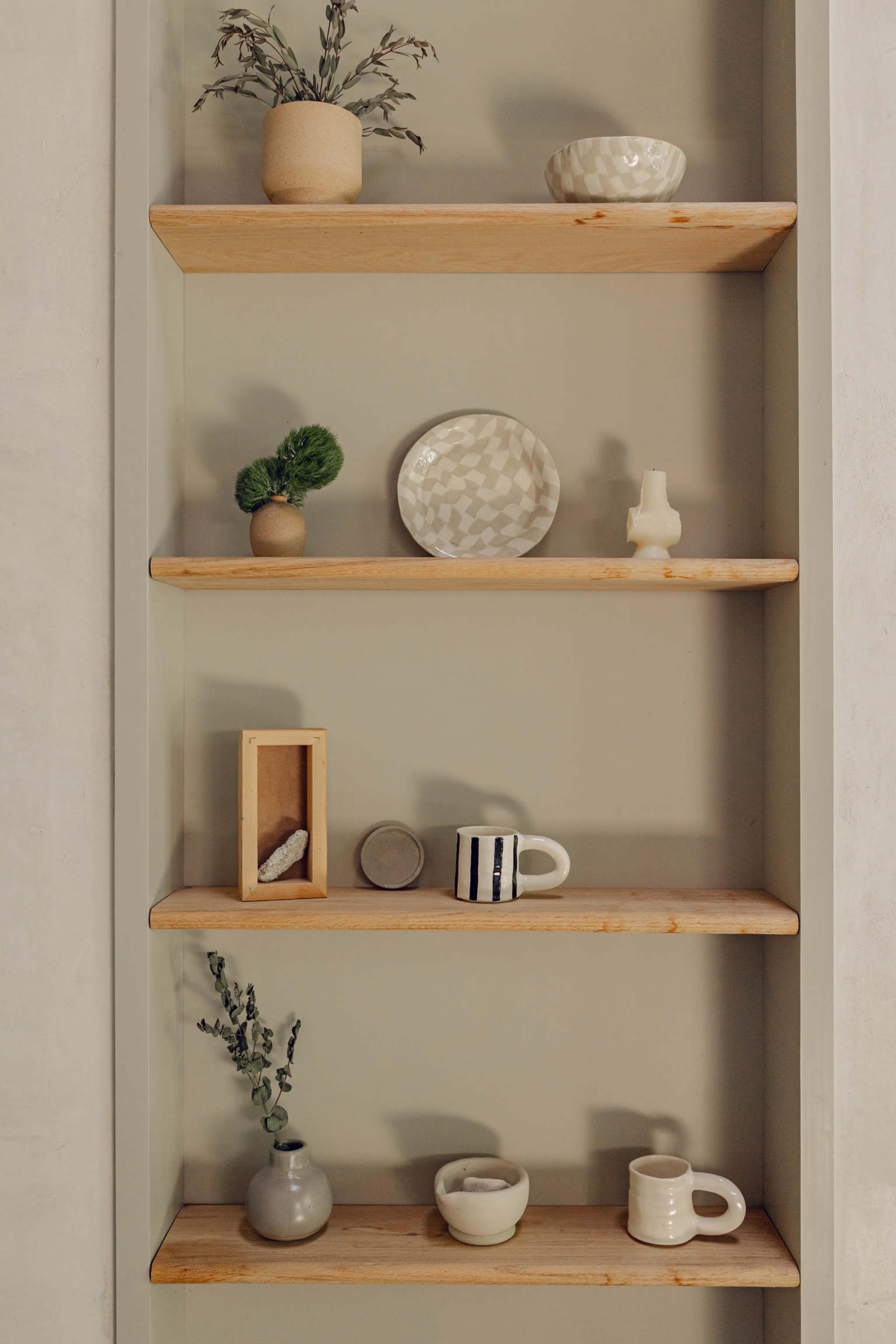The image shows a wall-mounted bookshelf with five wooden shelves displaying various decorative items, including bowls, vases, and mugs.