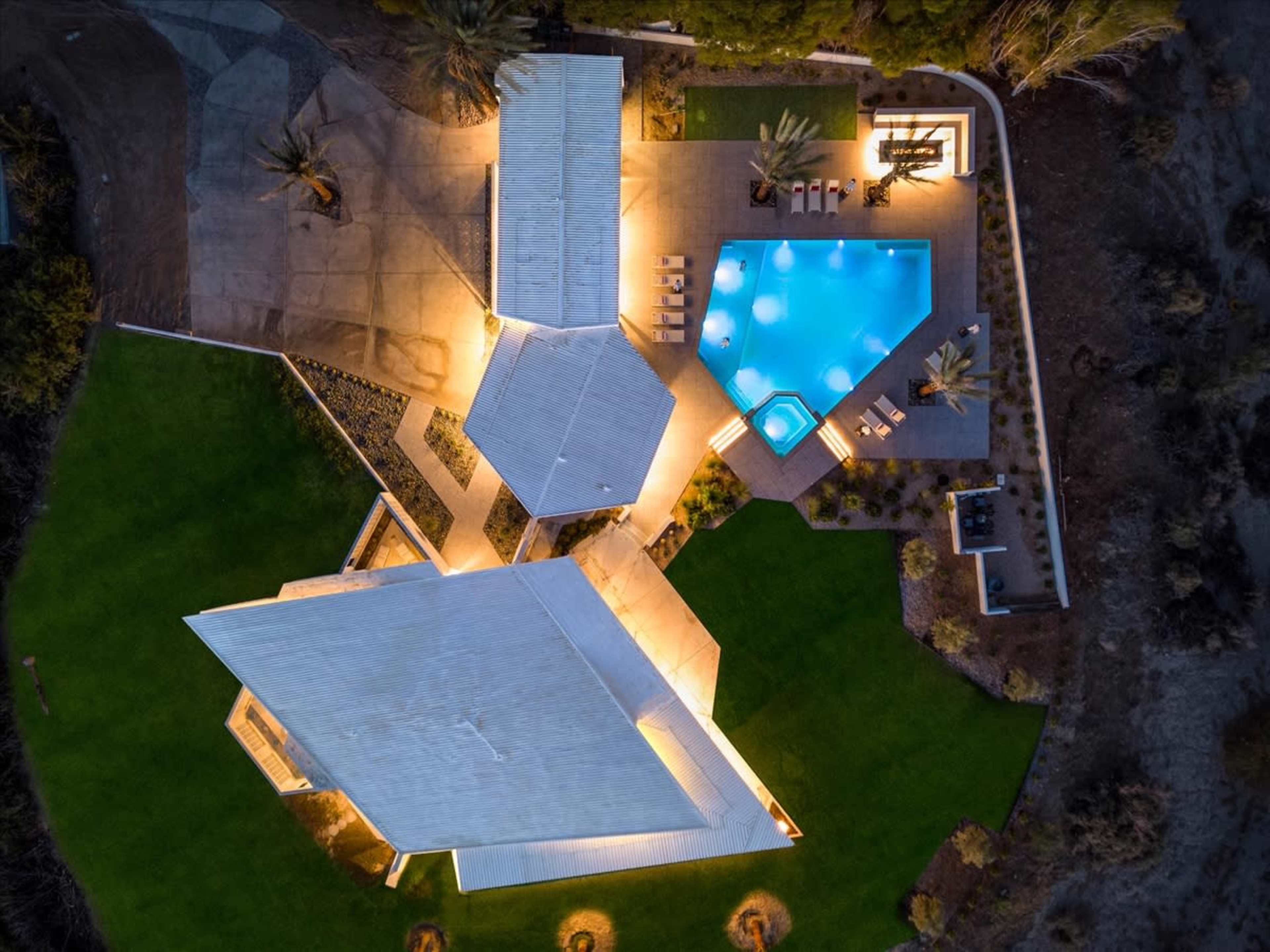 A modern architectural complex with three buildings surrounding a swimming pool and landscaped outdoor area, illuminated at night.