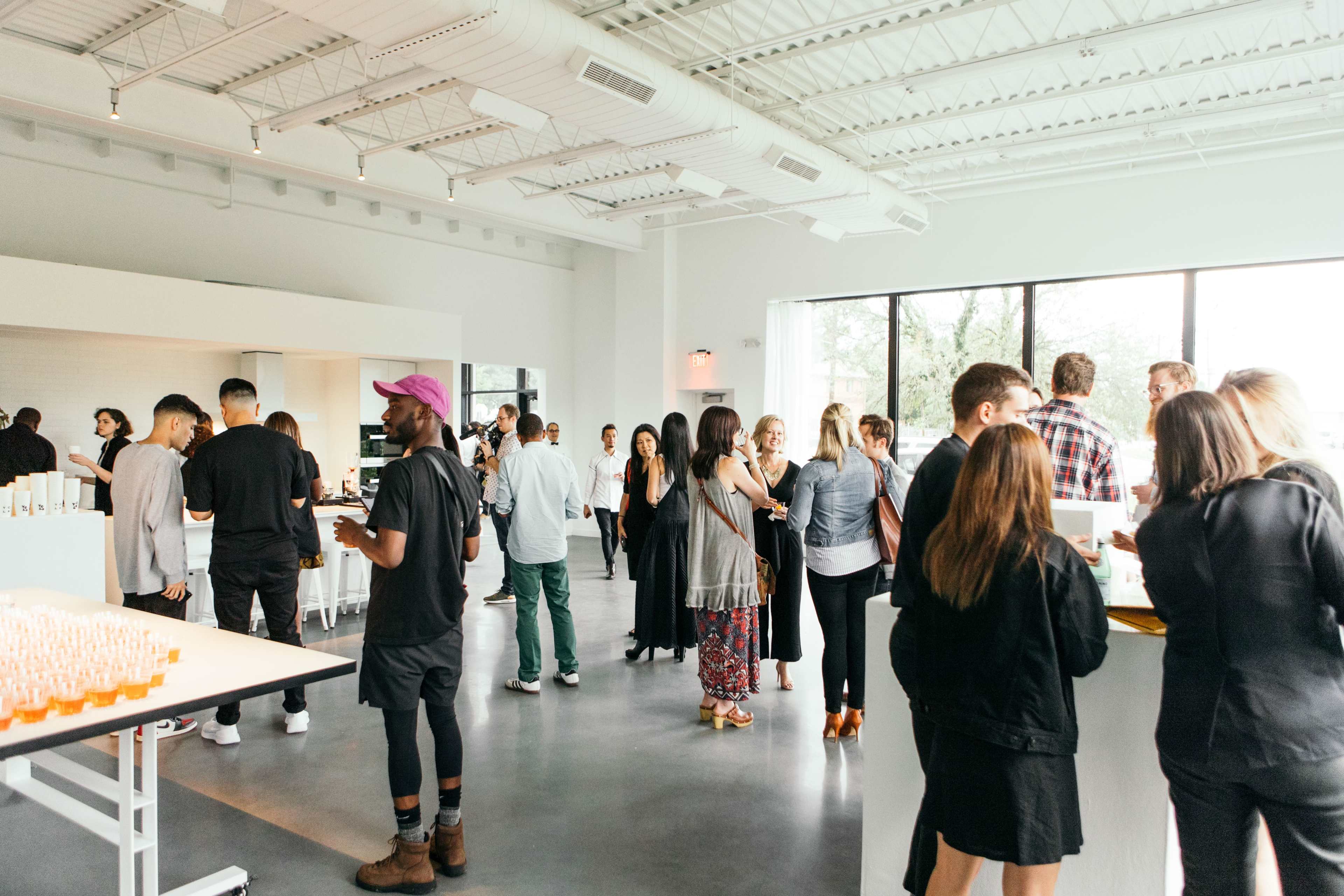 A group of people mingles and interacts in a modern, well-lit event space with large windows.