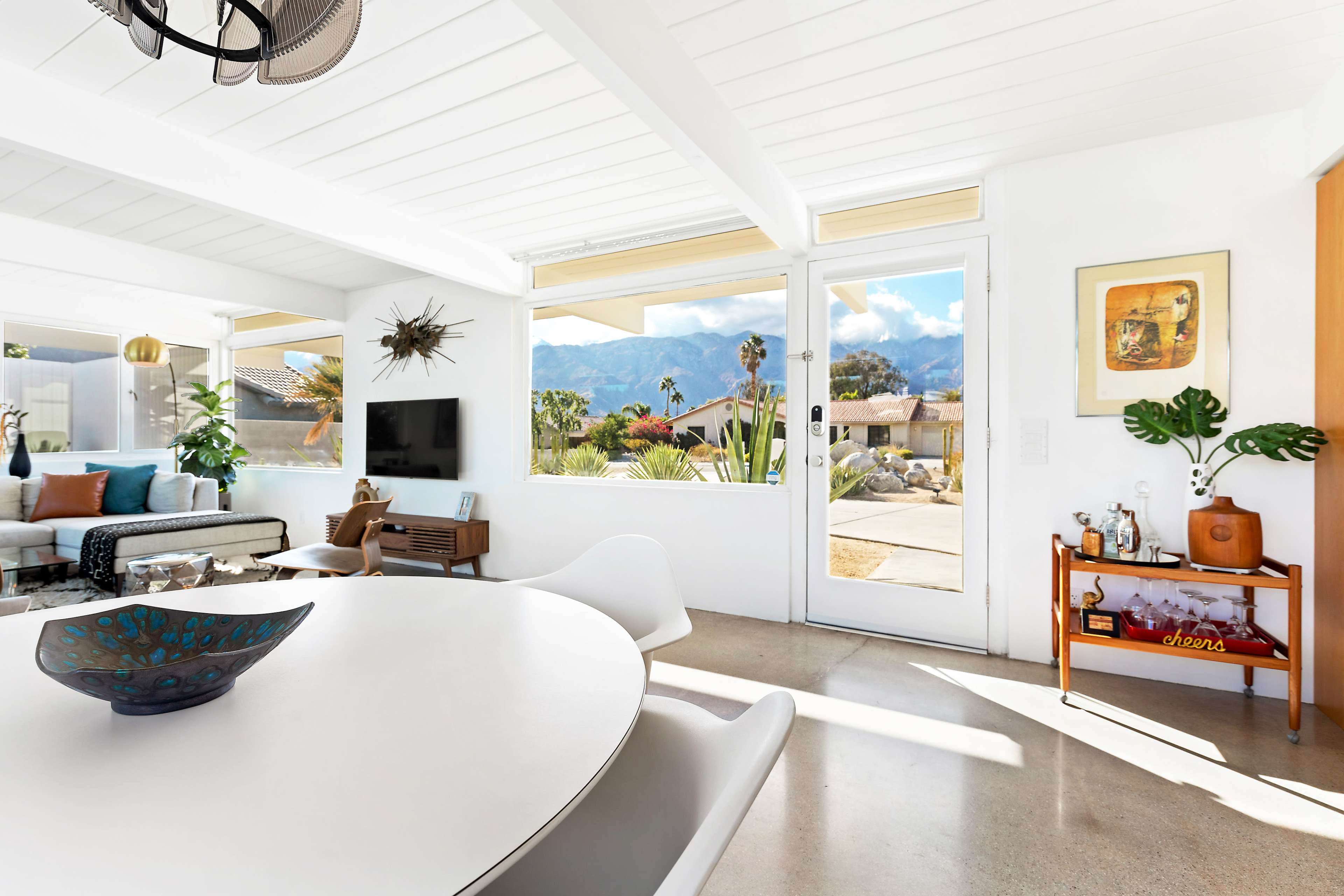 A modern living area features a round dining table, a comfortable sofa, and large windows that showcase a mountainous view.