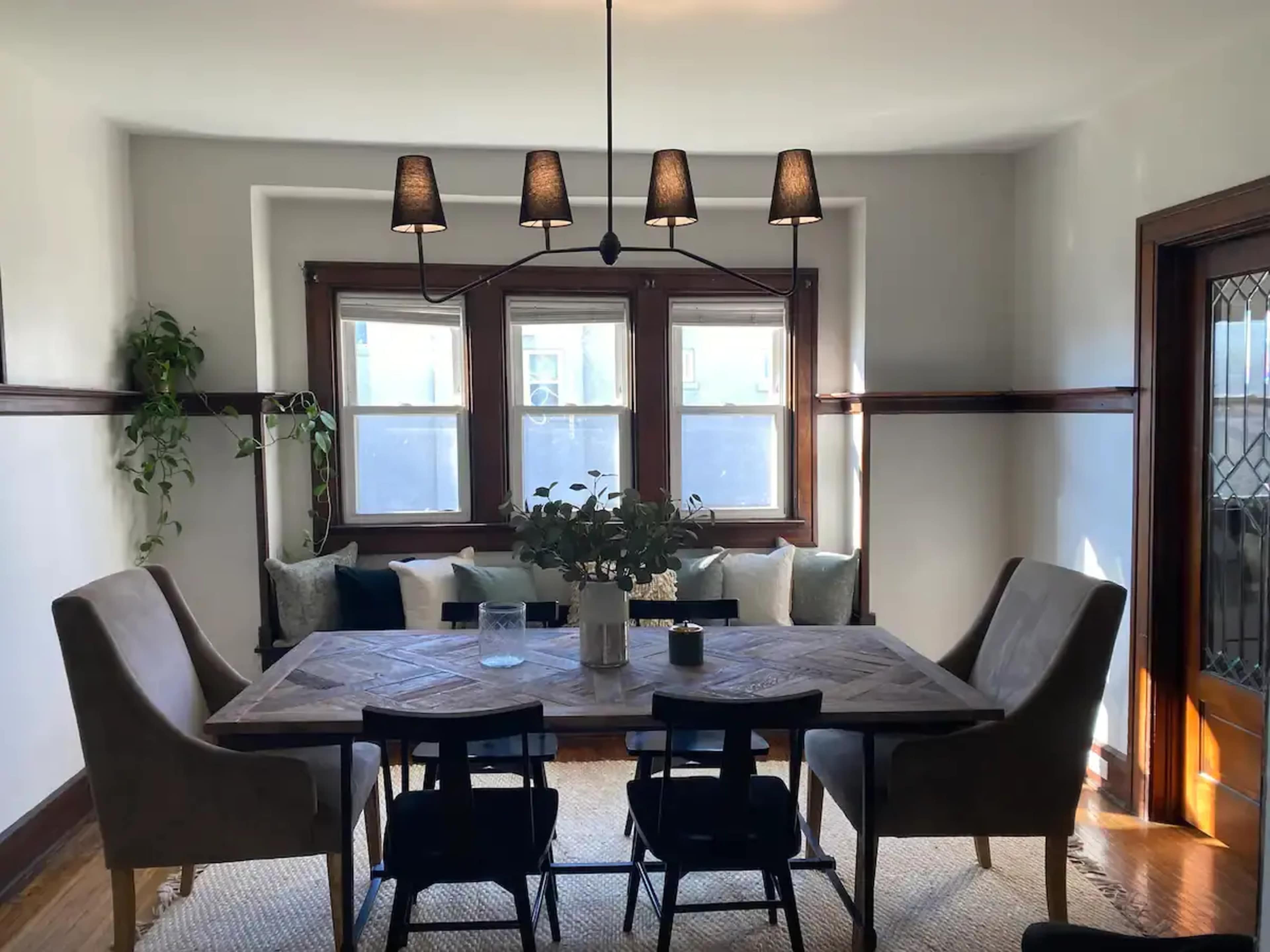 A dining area with a wooden table surrounded by upholstered and wooden chairs, illuminated by a hanging light fixture.
