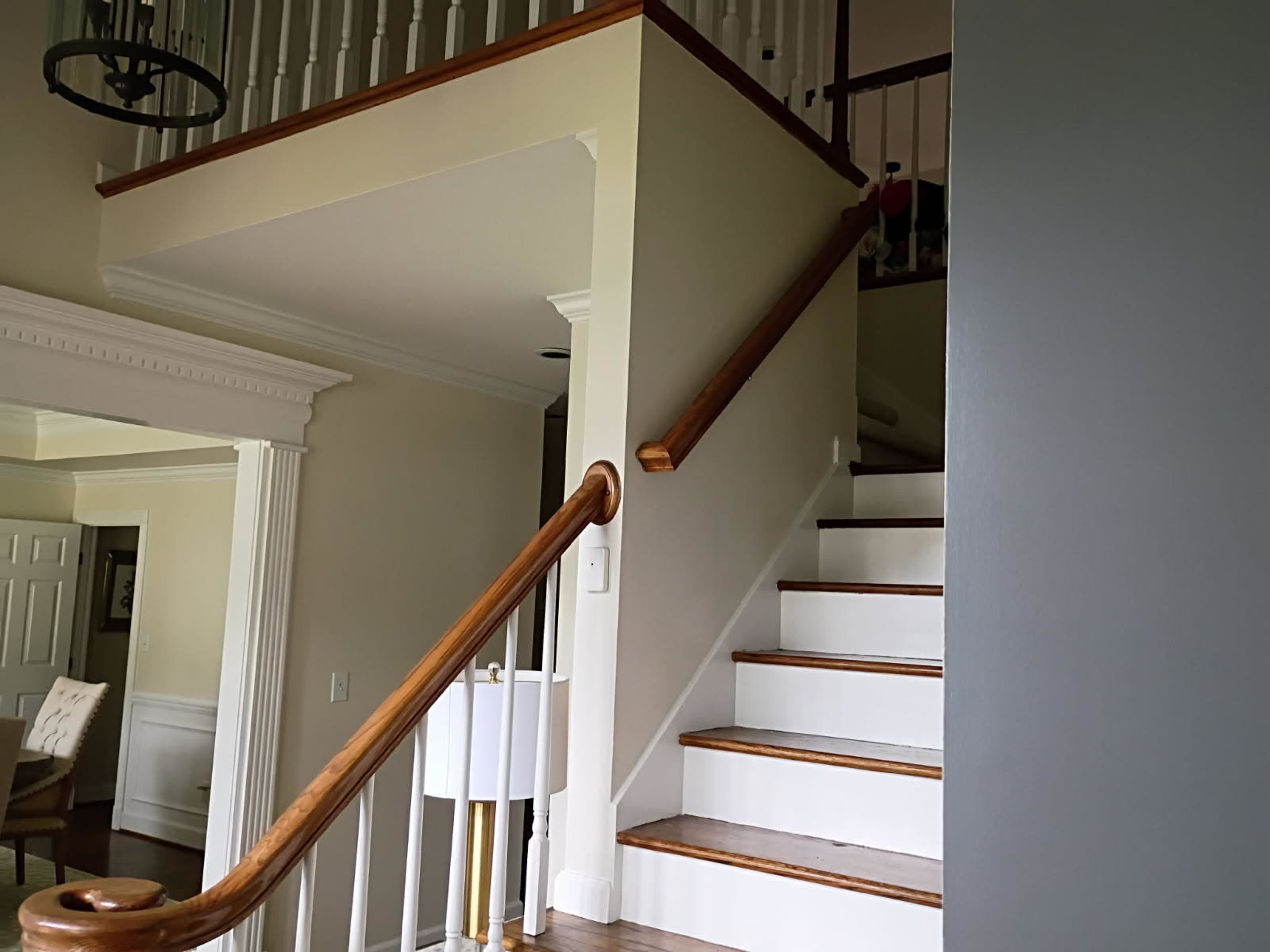 A staircase with white steps and a wooden handrail leads to an upper landing in a well-lit interior.