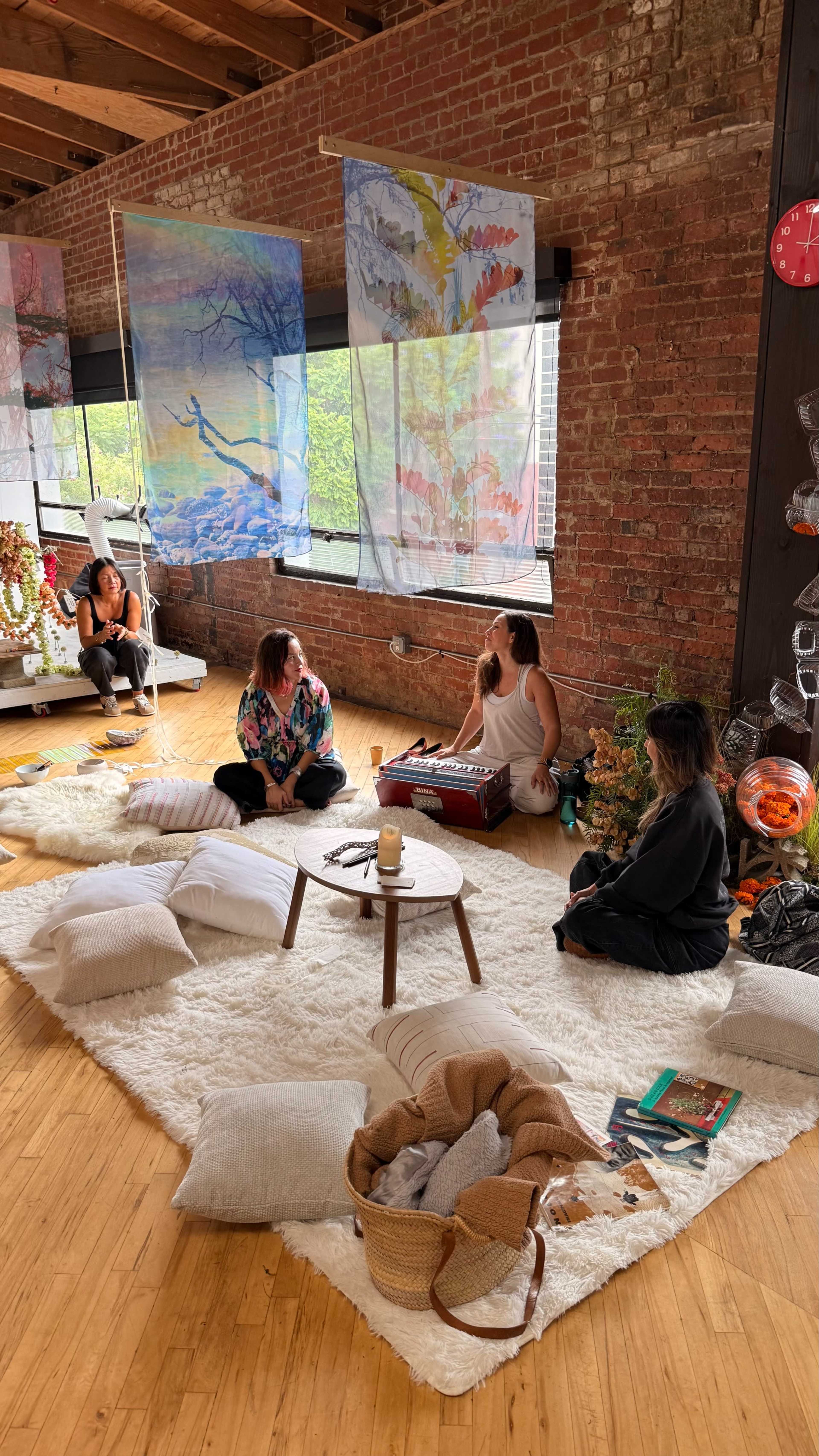 A group of four people sits in a cozy room with brick walls, surrounded by decorative banners, cushions, and a small coffee table.