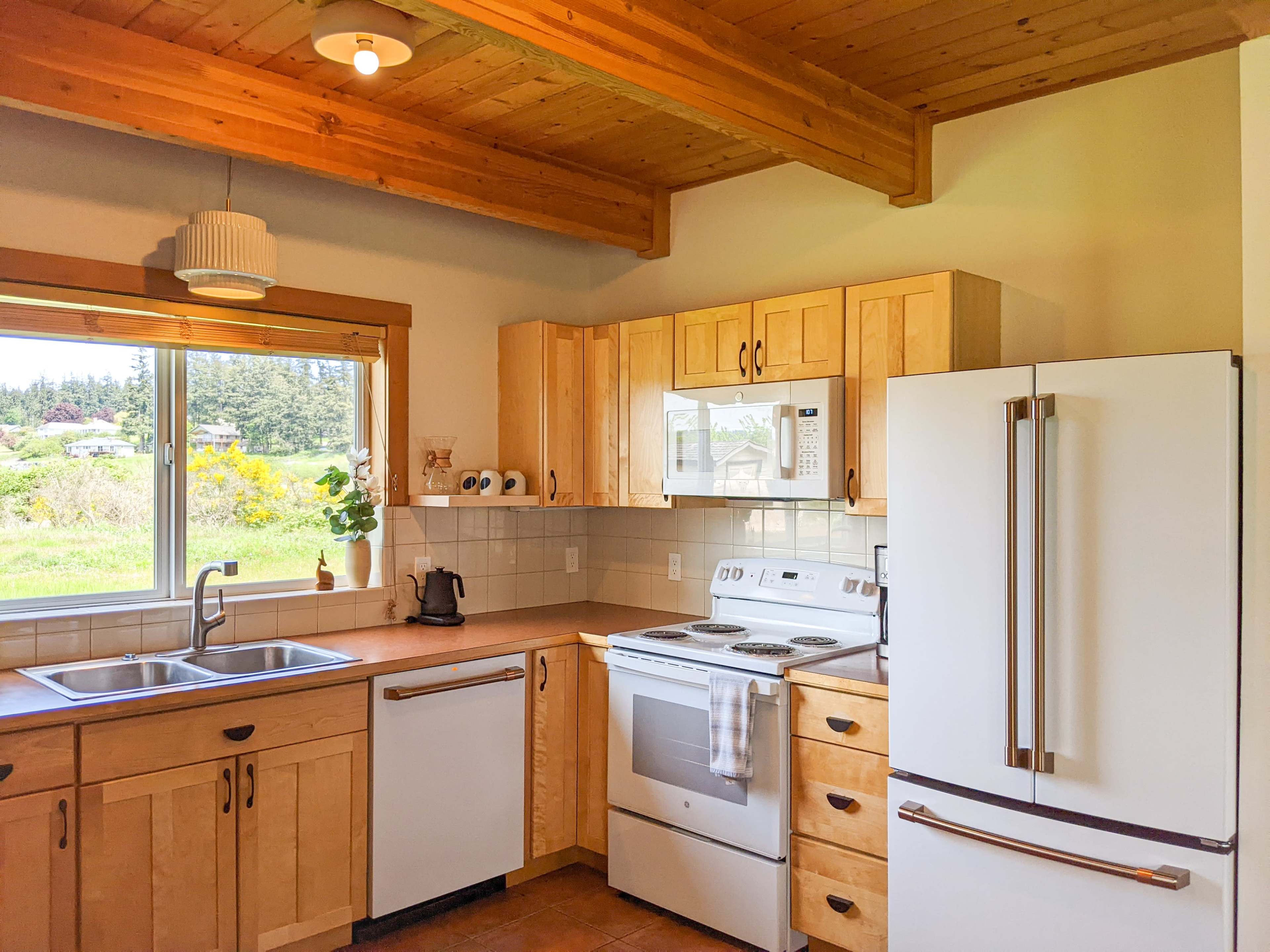 A modern kitchen featuring wooden cabinetry, stainless steel appliances, and a window with a view of the outdoors.