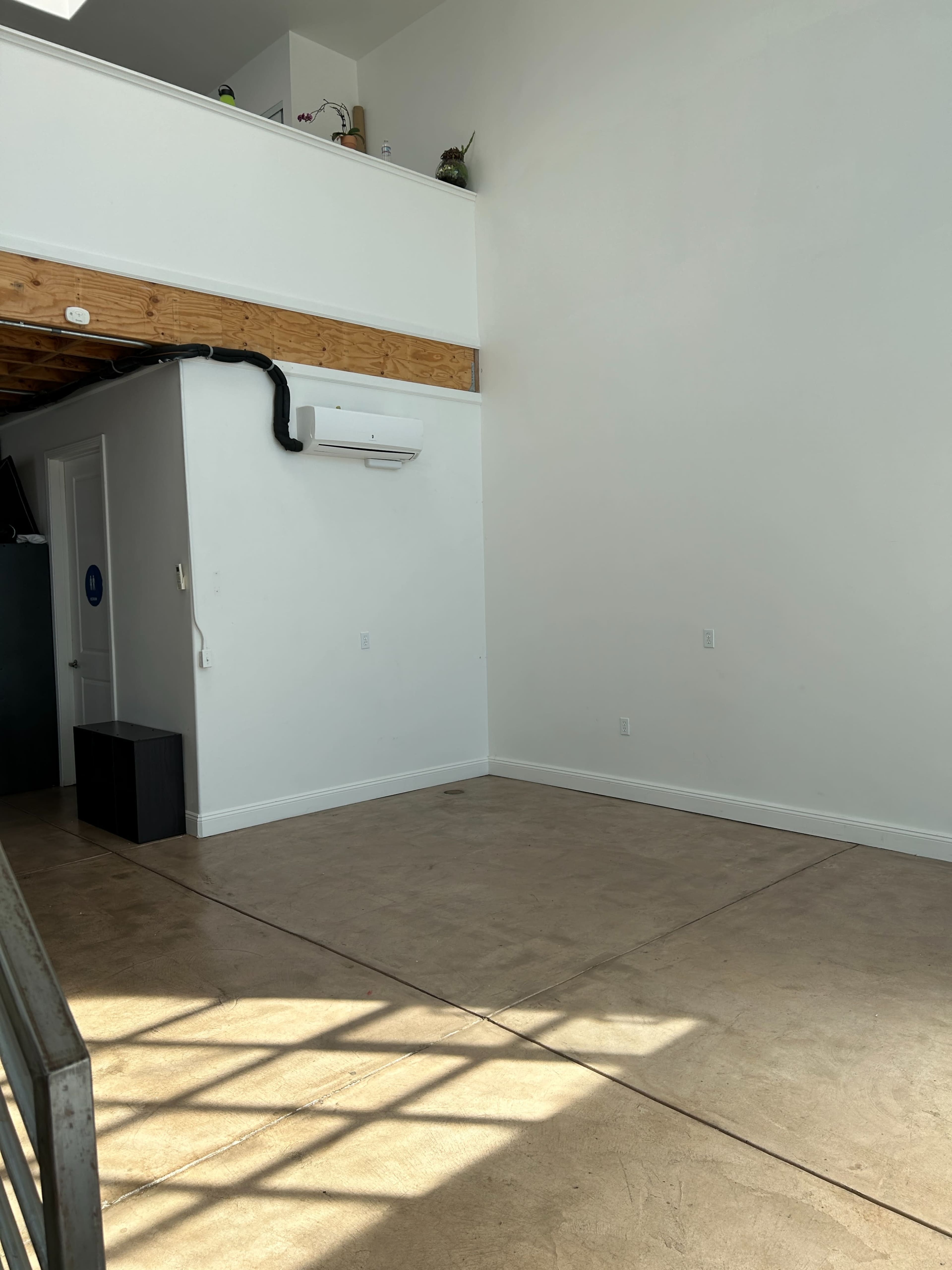 A spacious, empty room with a high ceiling and a concrete floor, illuminated by natural light.
