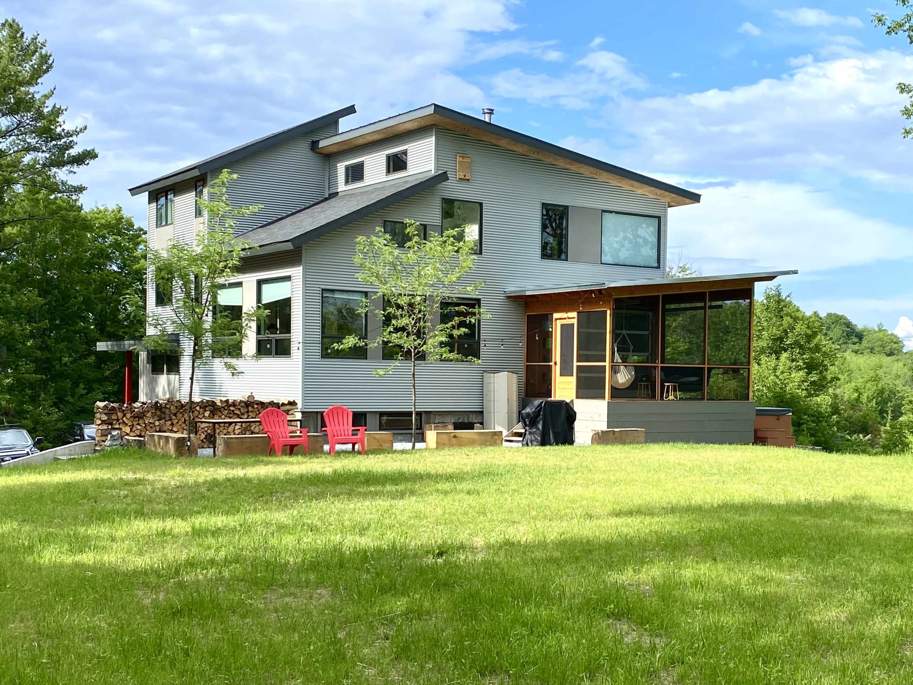 A modern house with large windows and a screened porch is set on a grassy lot surrounded by trees.