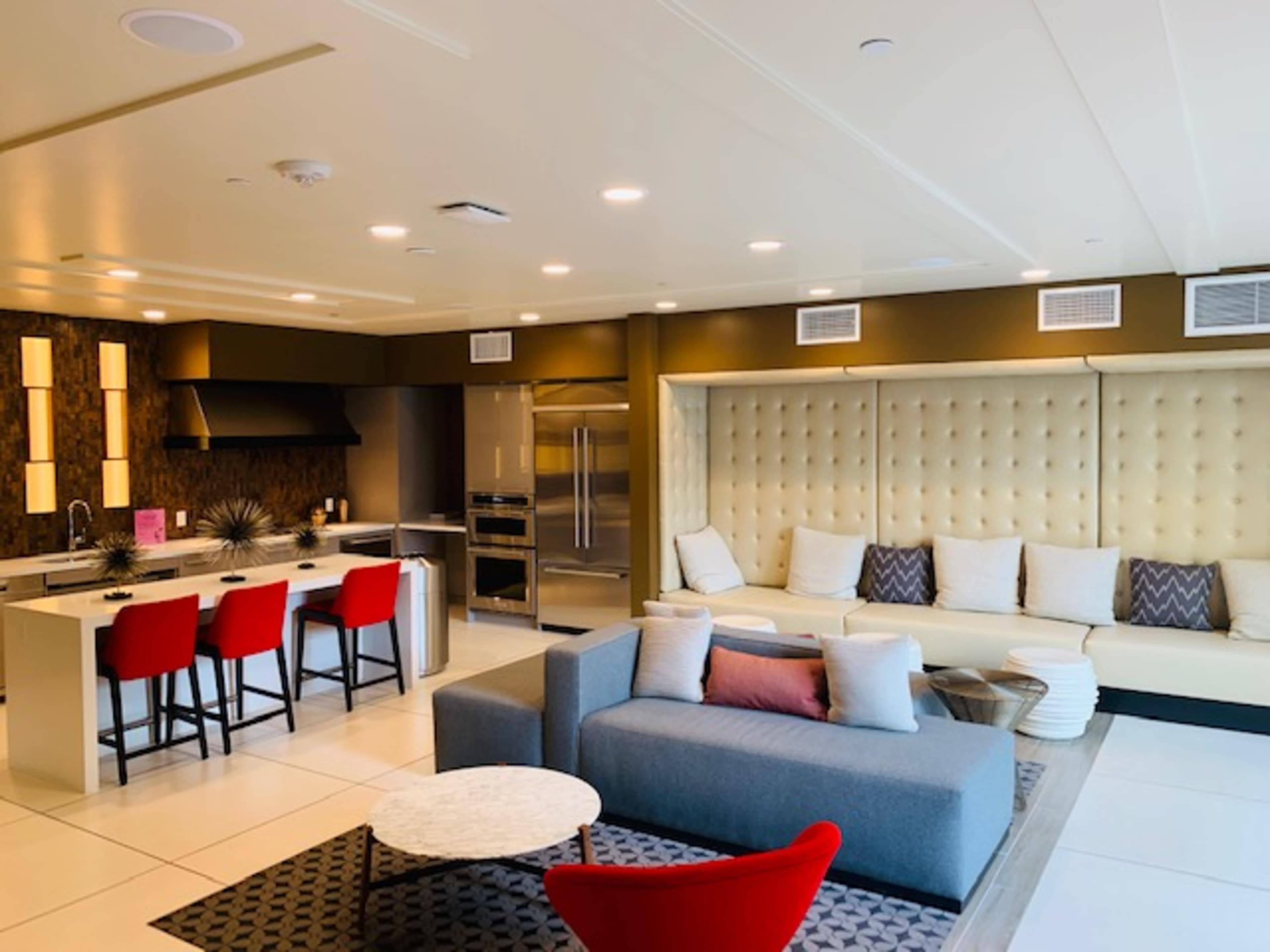 A modern living space featuring a kitchen with red bar stools, a sectional sofa, and a coffee table on a patterned rug.