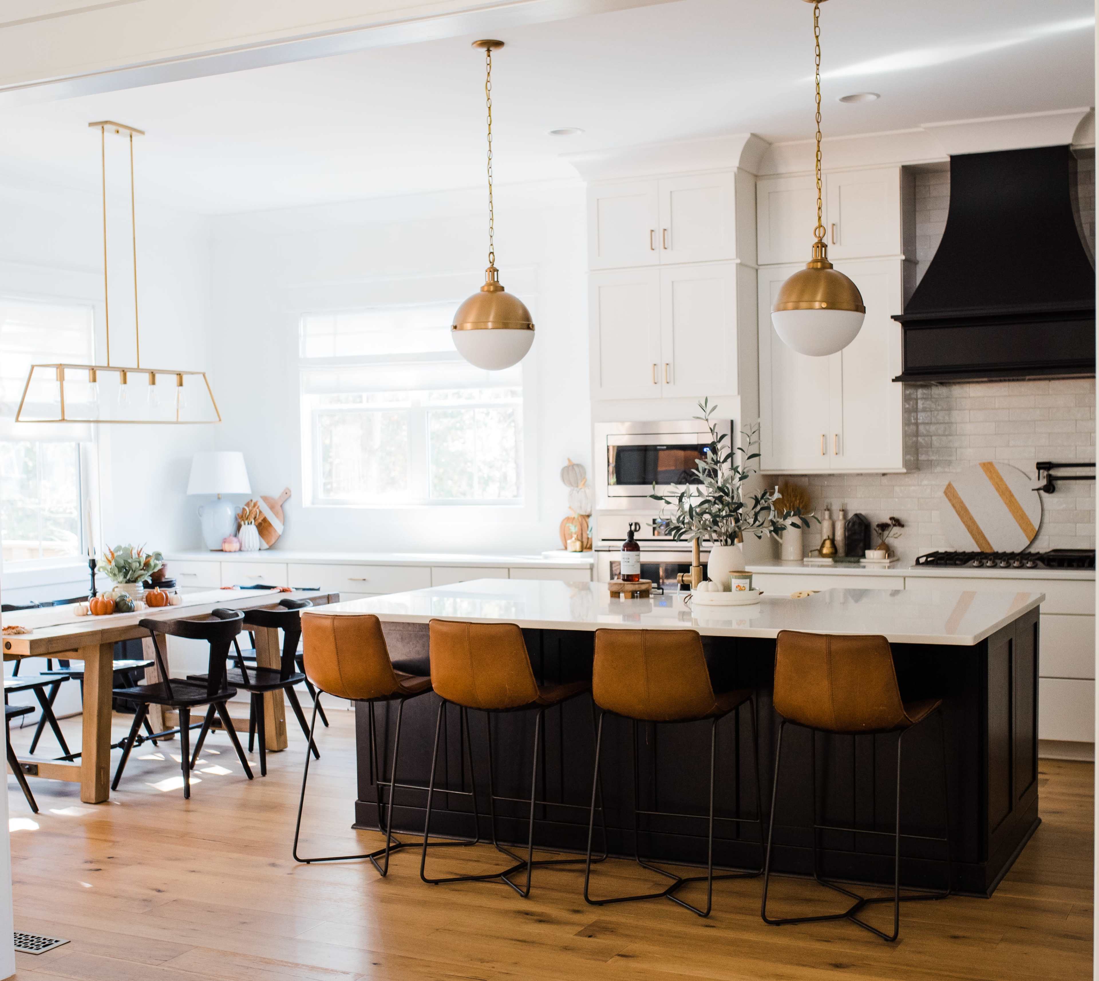 A modern kitchen with a large island featuring brown bar stools, a wooden dining table, and pendant lighting.