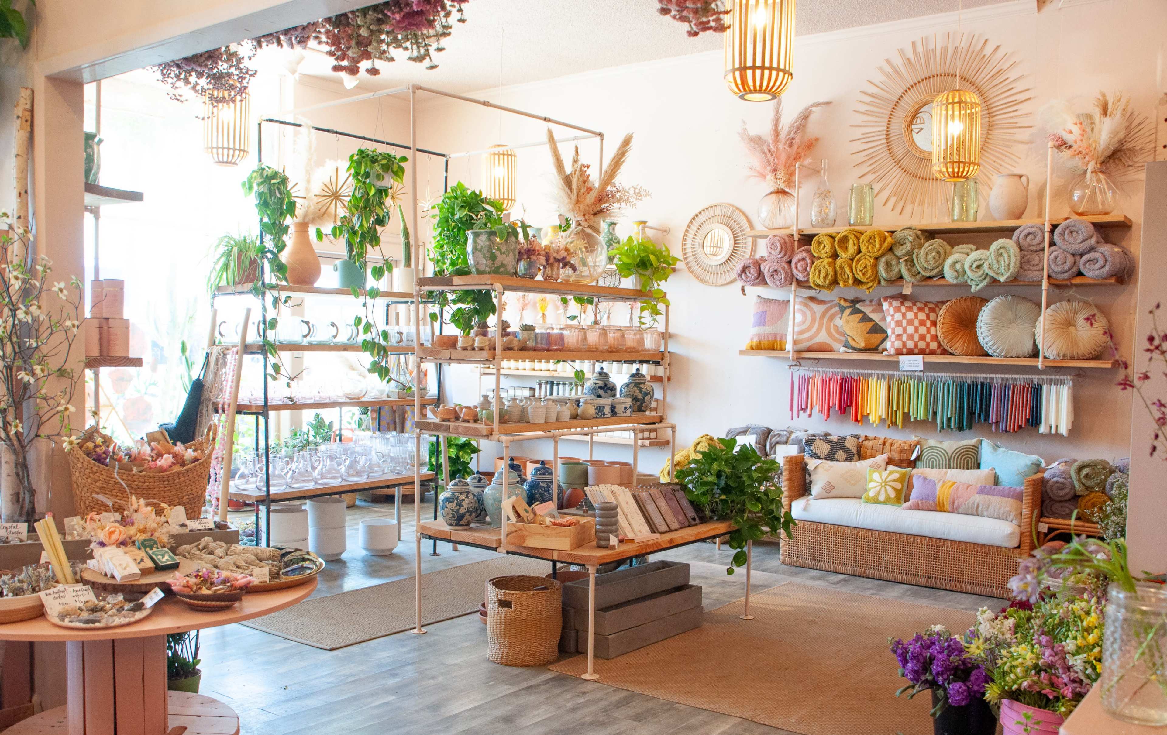A cozy shop filled with neatly arranged shelves of plants, home goods, and colorful textiles, accompanied by a comfortable seating area.