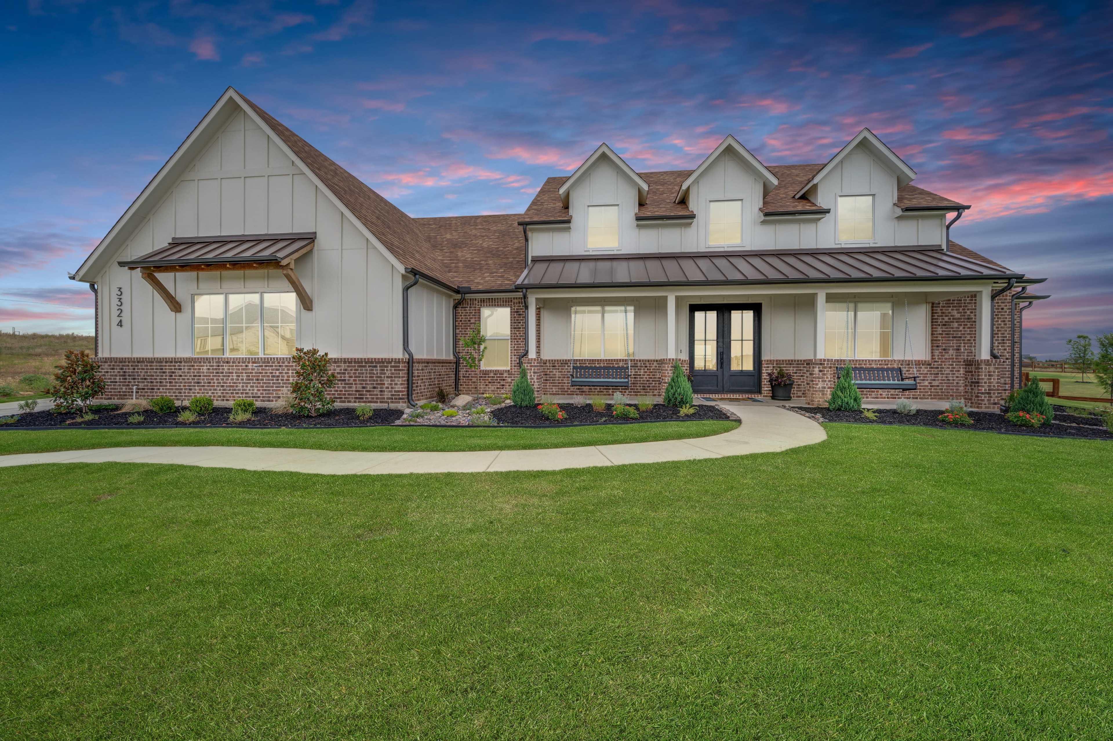 A two-story house with a combination of brick and siding sits on a manicured lawn, featuring multiple gabled roofs and a curved walkway leading to the front door.