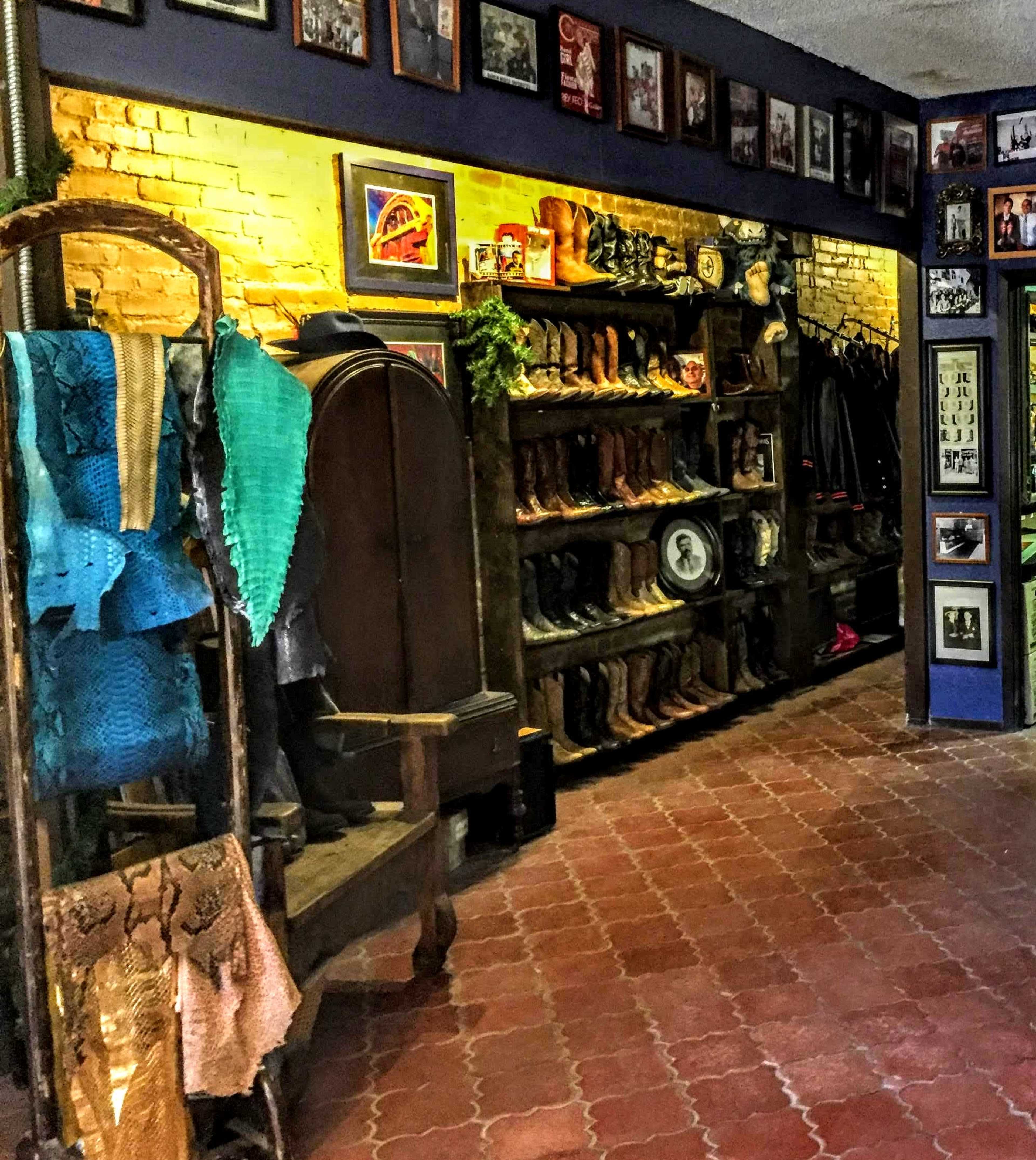 The image shows a shop interior with shelves filled with various styles of boots, framed photographs on the walls, and clothing displayed on a wooden rack.