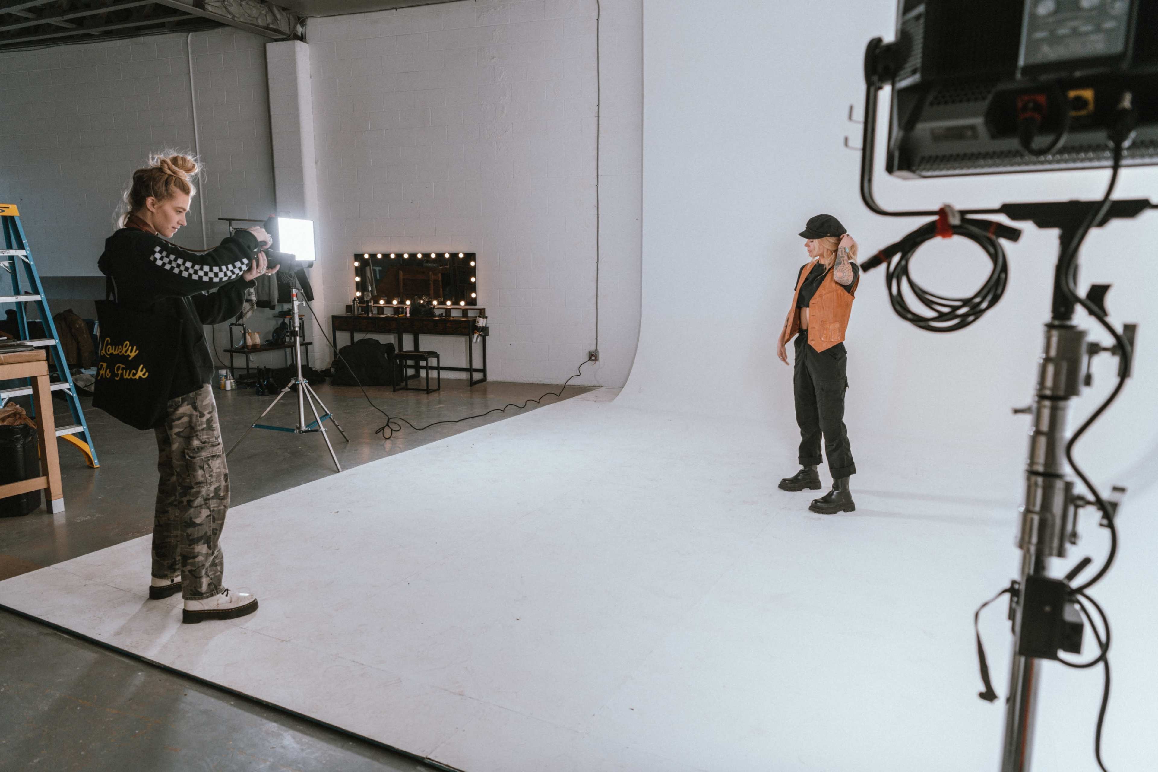 A photographer captures a model posing in front of a plain white backdrop in a studio.