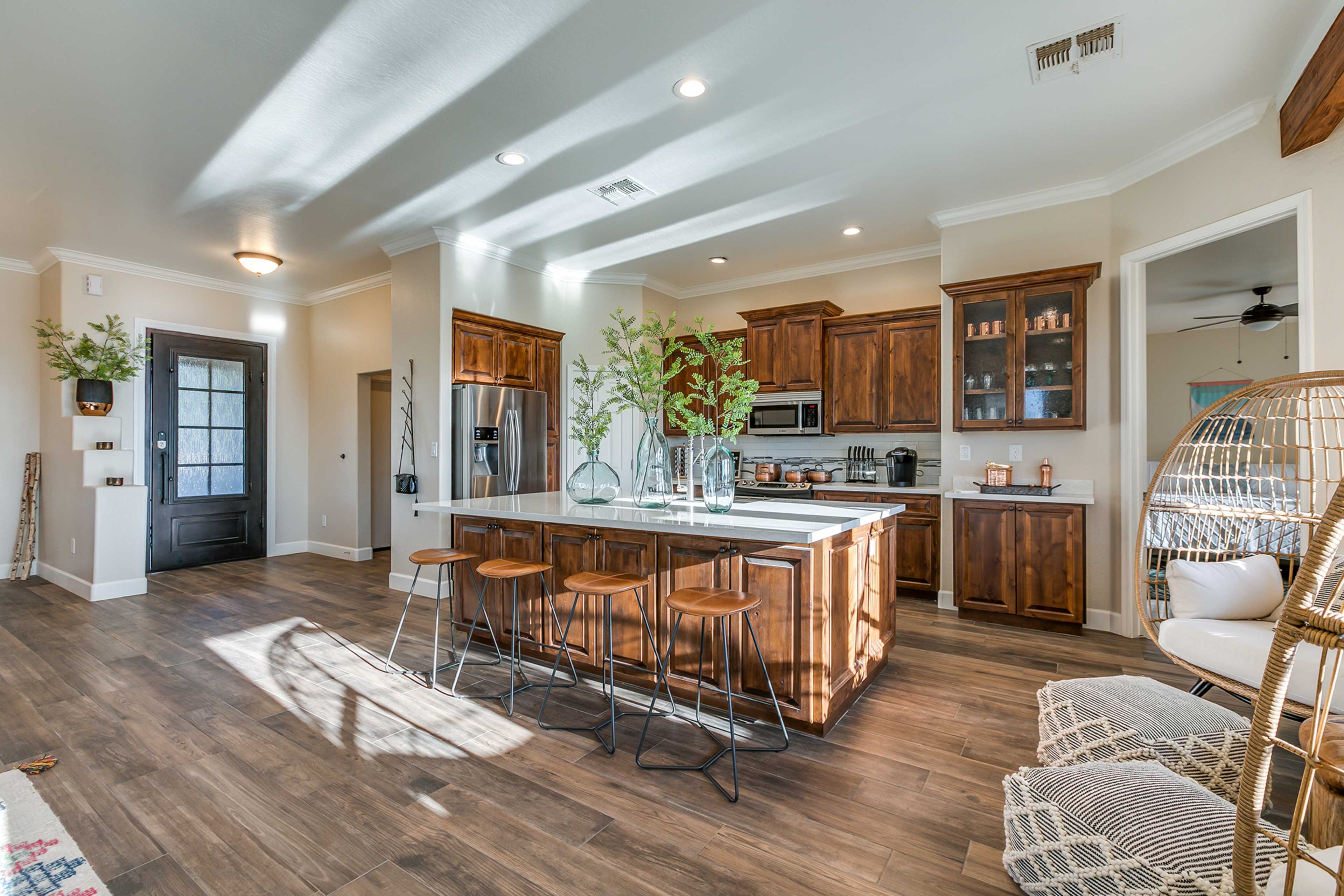 A modern kitchen features wooden cabinets, a large island with bar seating, and natural light streaming through the windows.
