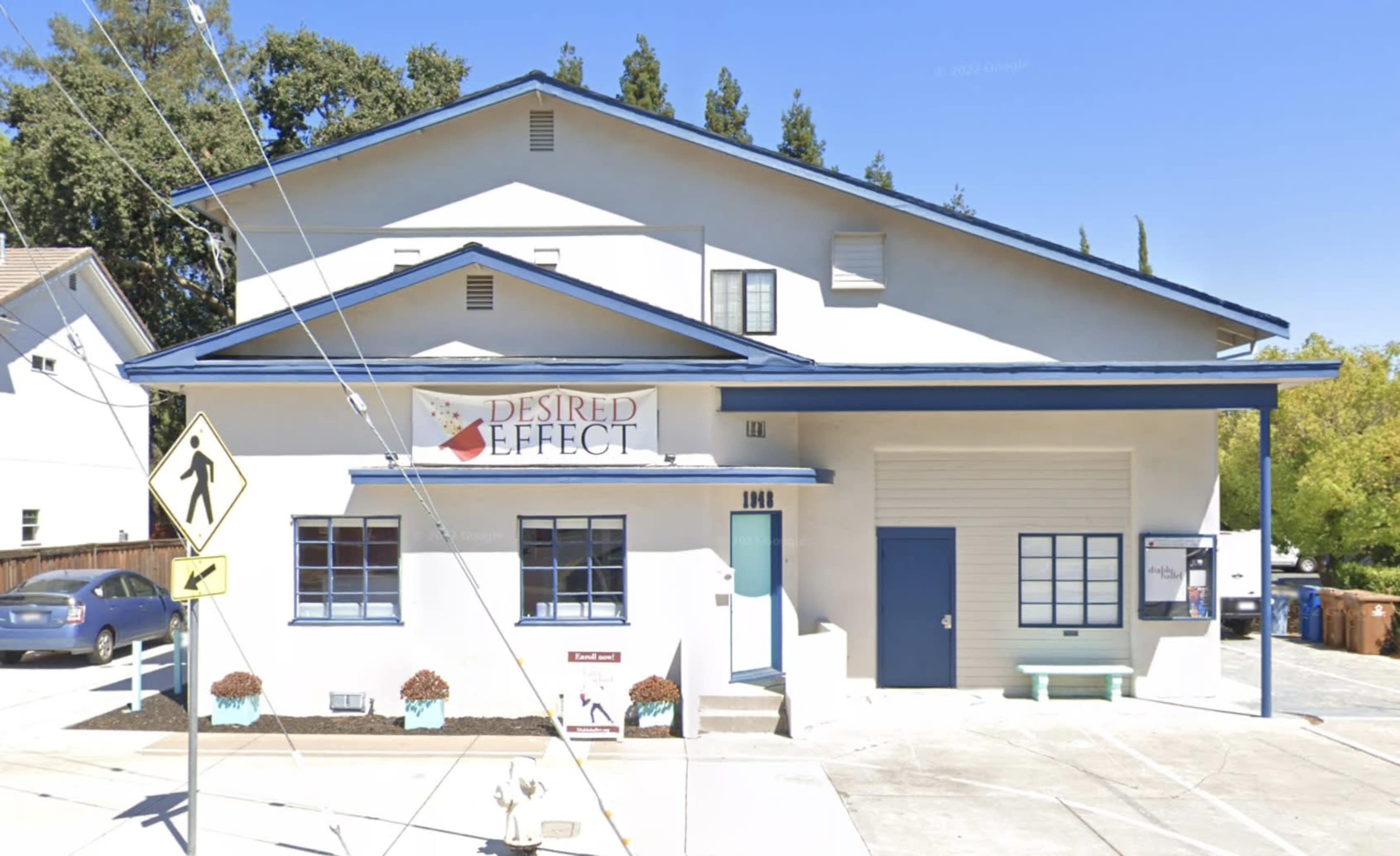 A two-story commercial building with a blue roof and a sign that reads "Desired Effect," along with a pedestrian crossing sign in front.