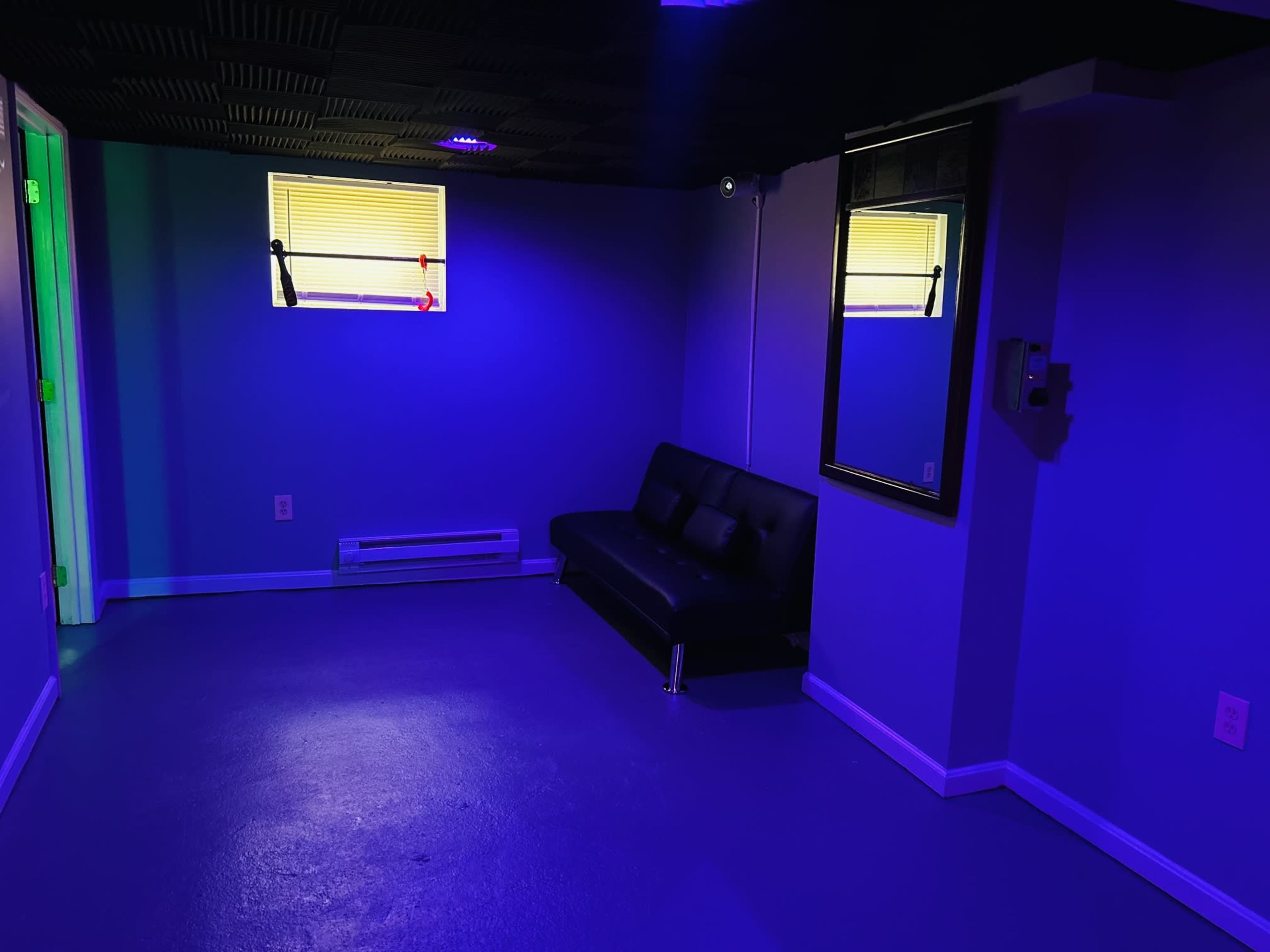 The image shows a dimly lit room with purple walls, a black sofa, a mirror, and a window with yellow blinds.