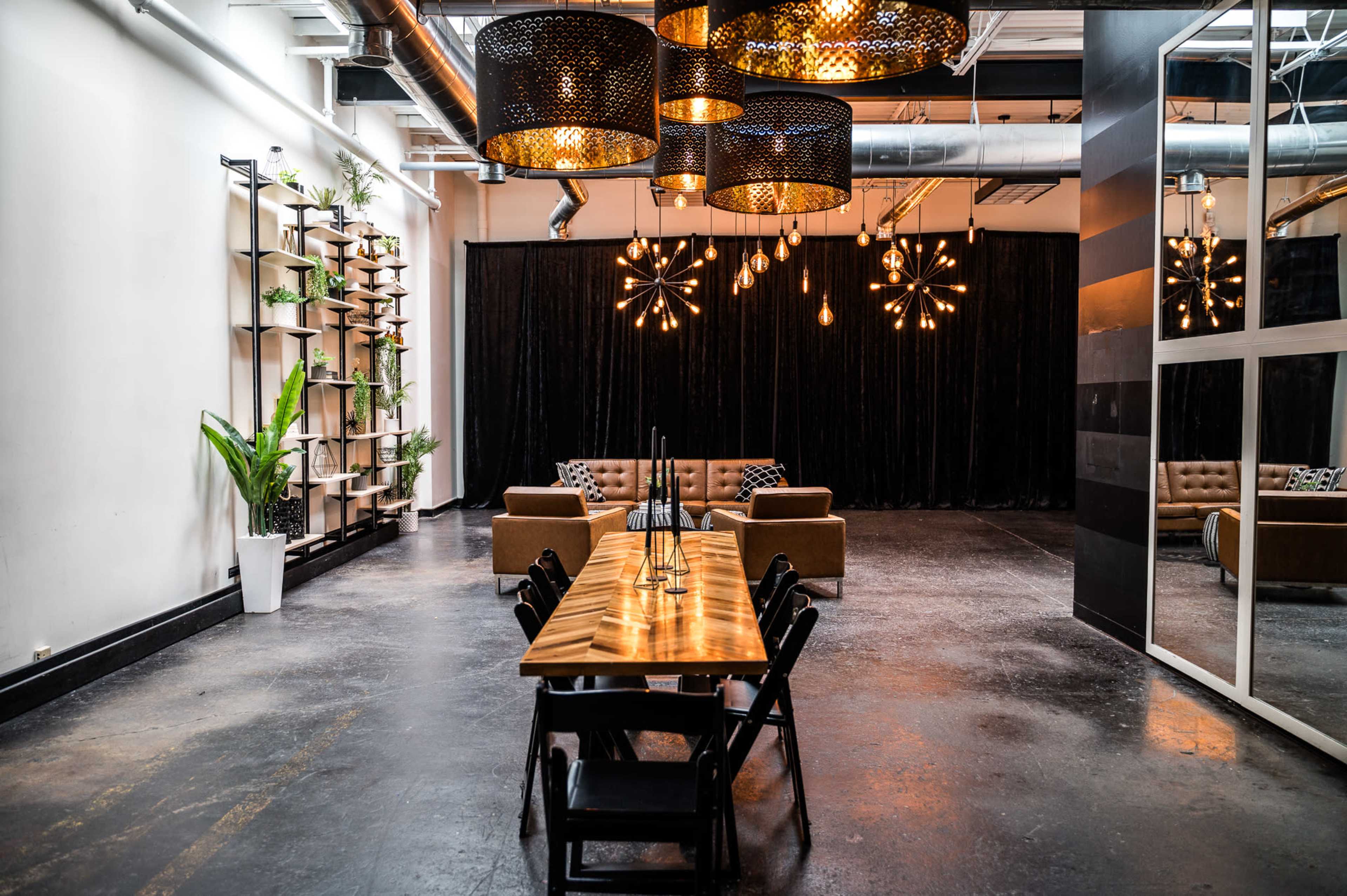 A modern interior space featuring a long wooden dining table surrounded by black chairs, a stylish couch, and decorative lighting fixtures.