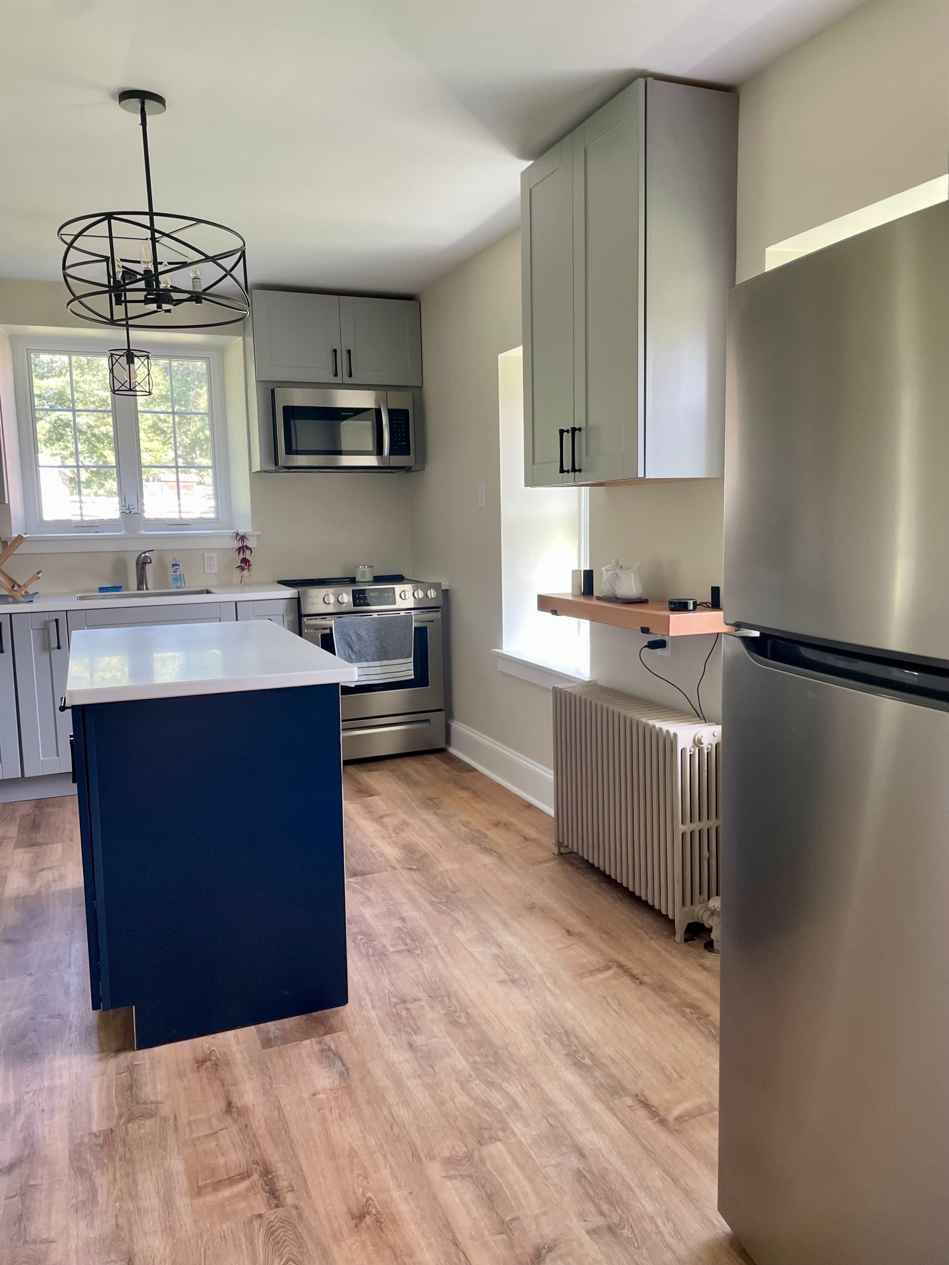 A modern kitchen featuring stainless steel appliances, a central island with a blue base, and light wood flooring.