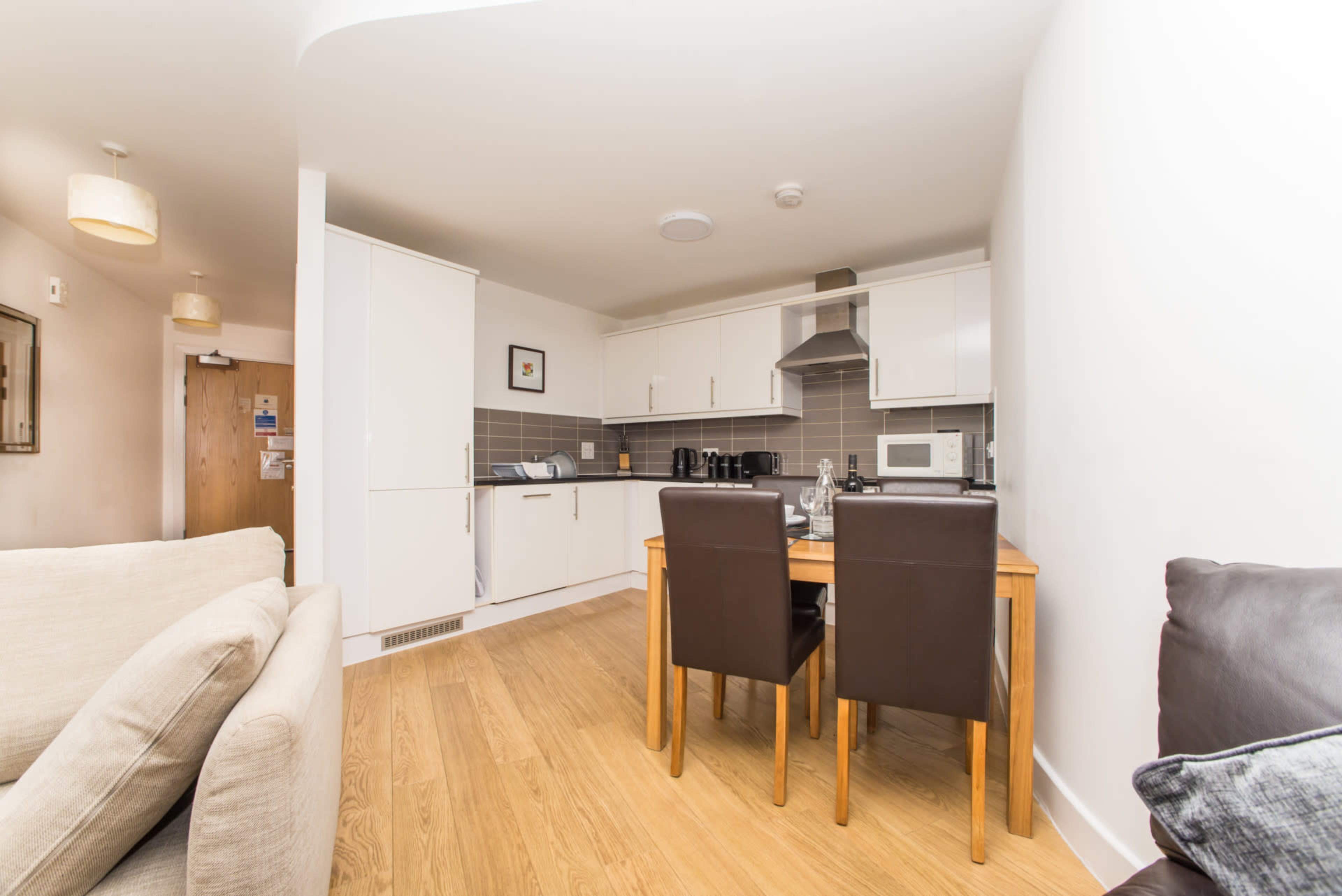 A modern kitchen and dining area with a wooden table and two brown chairs, adjacent to light-colored walls and cabinetry.