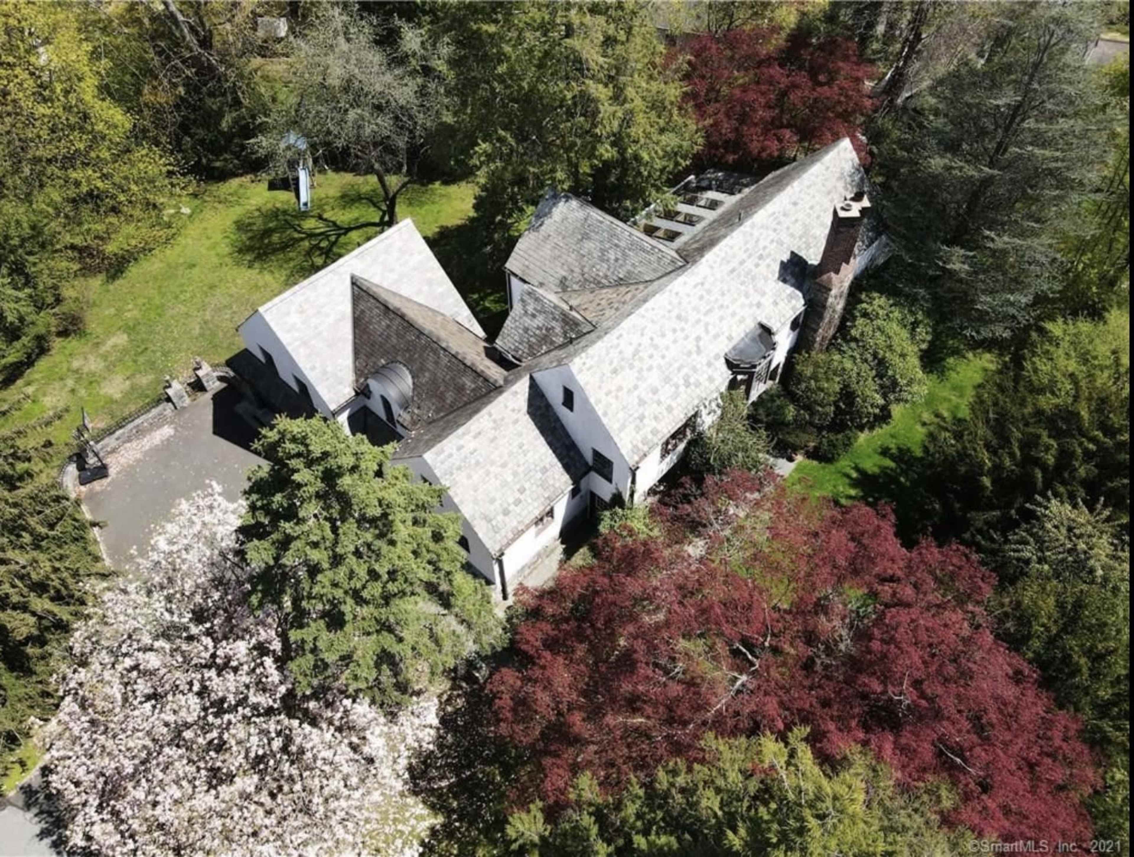 An aerial view of a unique, angled-roof house surrounded by colorful trees and lush greenery.