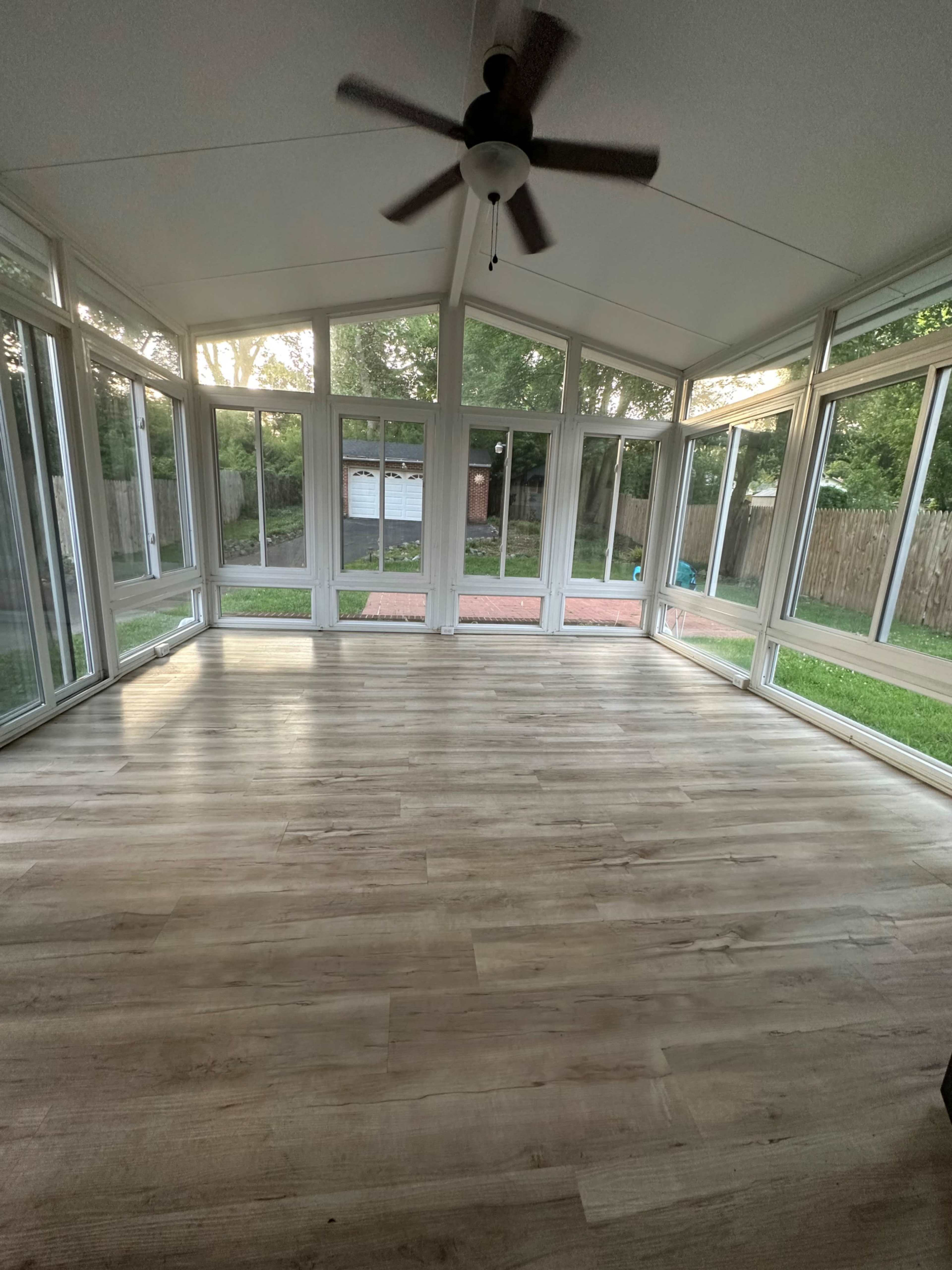 A spacious sunroom with large windows and a wooden floor, illuminated by natural light.