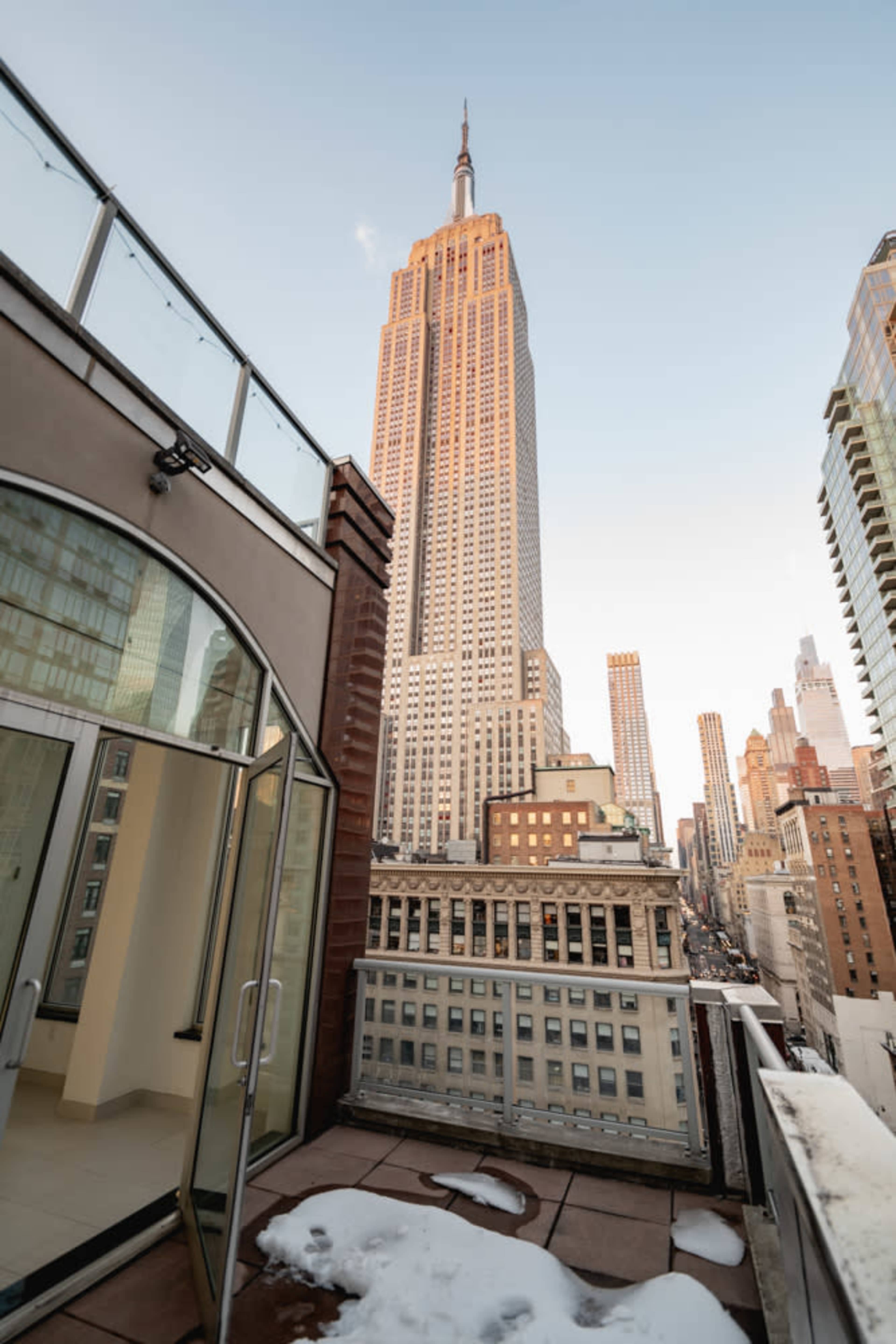 A view from a rooftop terrace overlooking the Empire State Building amidst a city skyline.