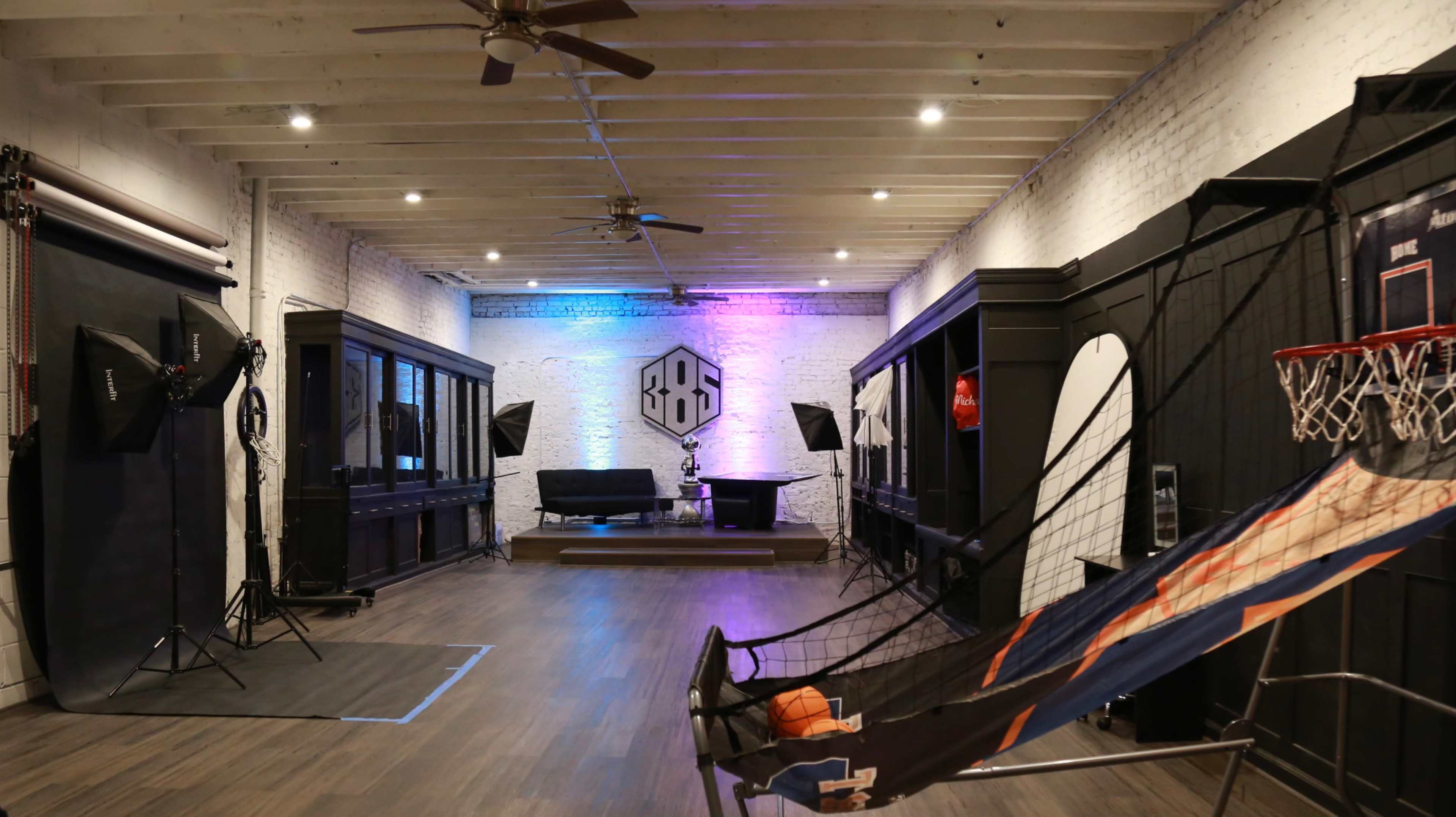 A spacious studio with a basketball hoop, photography equipment, and a seating area illuminated by colored lights.