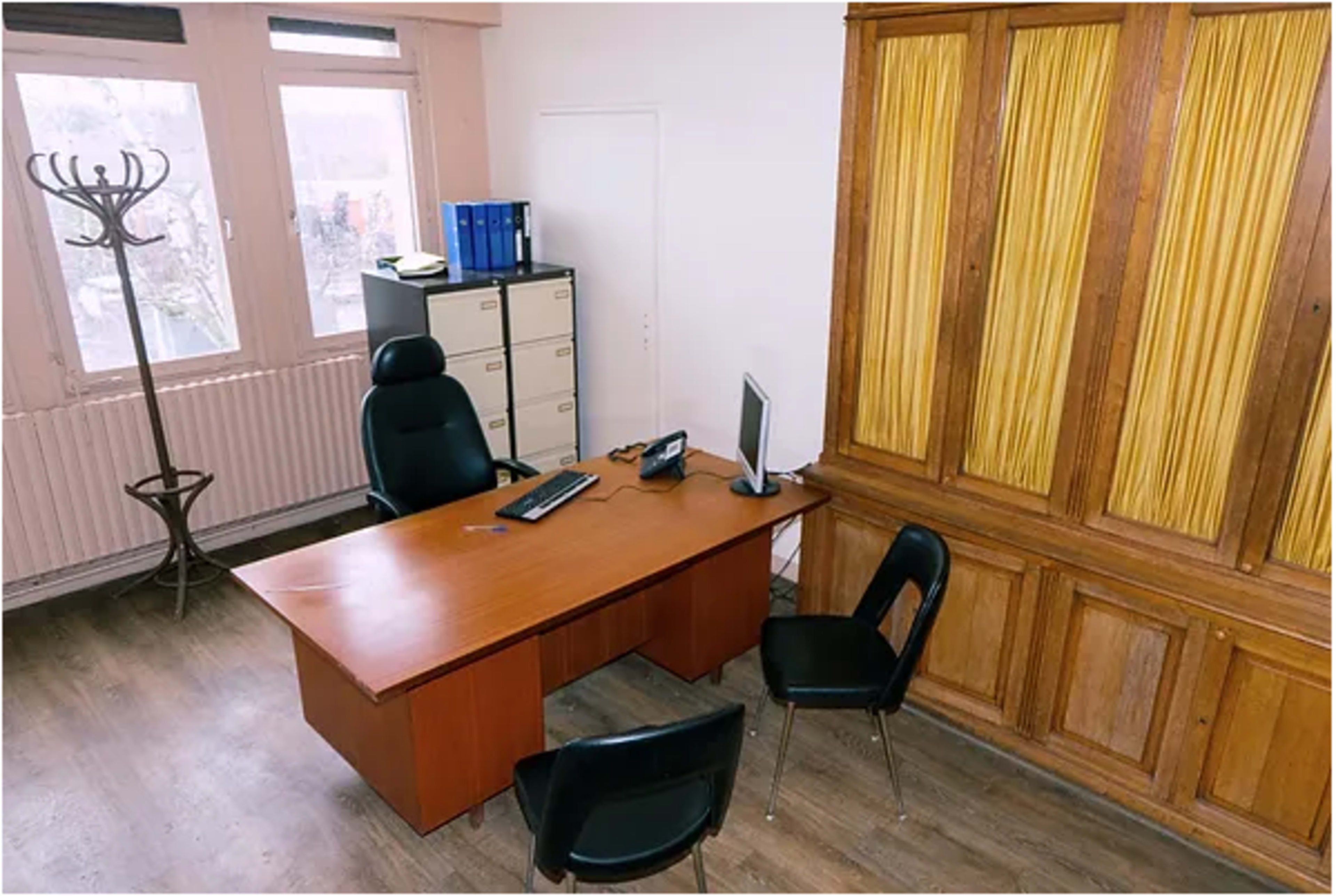 An office with a wooden desk, two black chairs, a computer monitor, and a wooden cabinet against the wall.