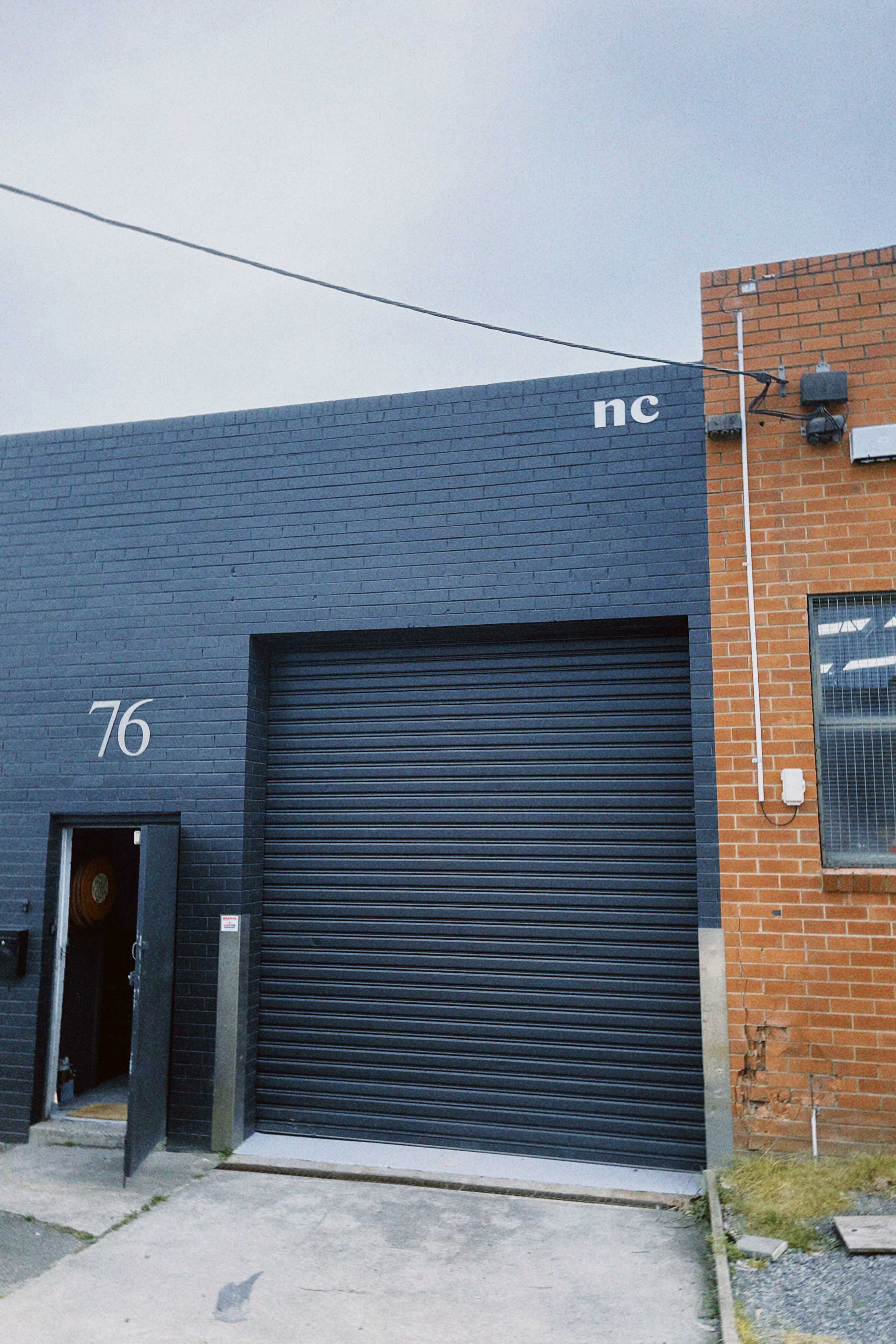A gray building with a roll-up door labeled "76" and the letters "nc" near the top.