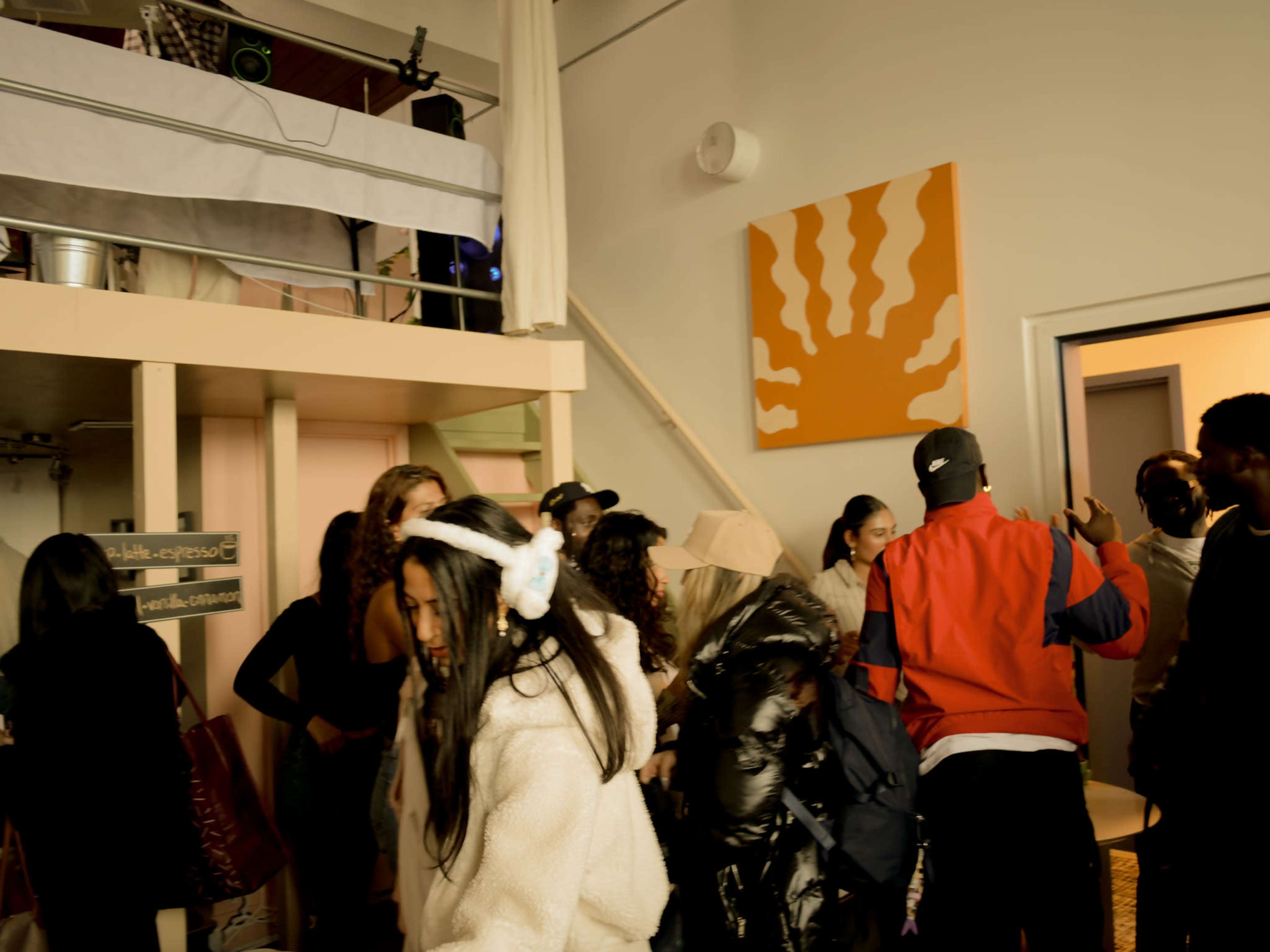 A crowd of people socialize in a room with a lofted area and colorful wall art.