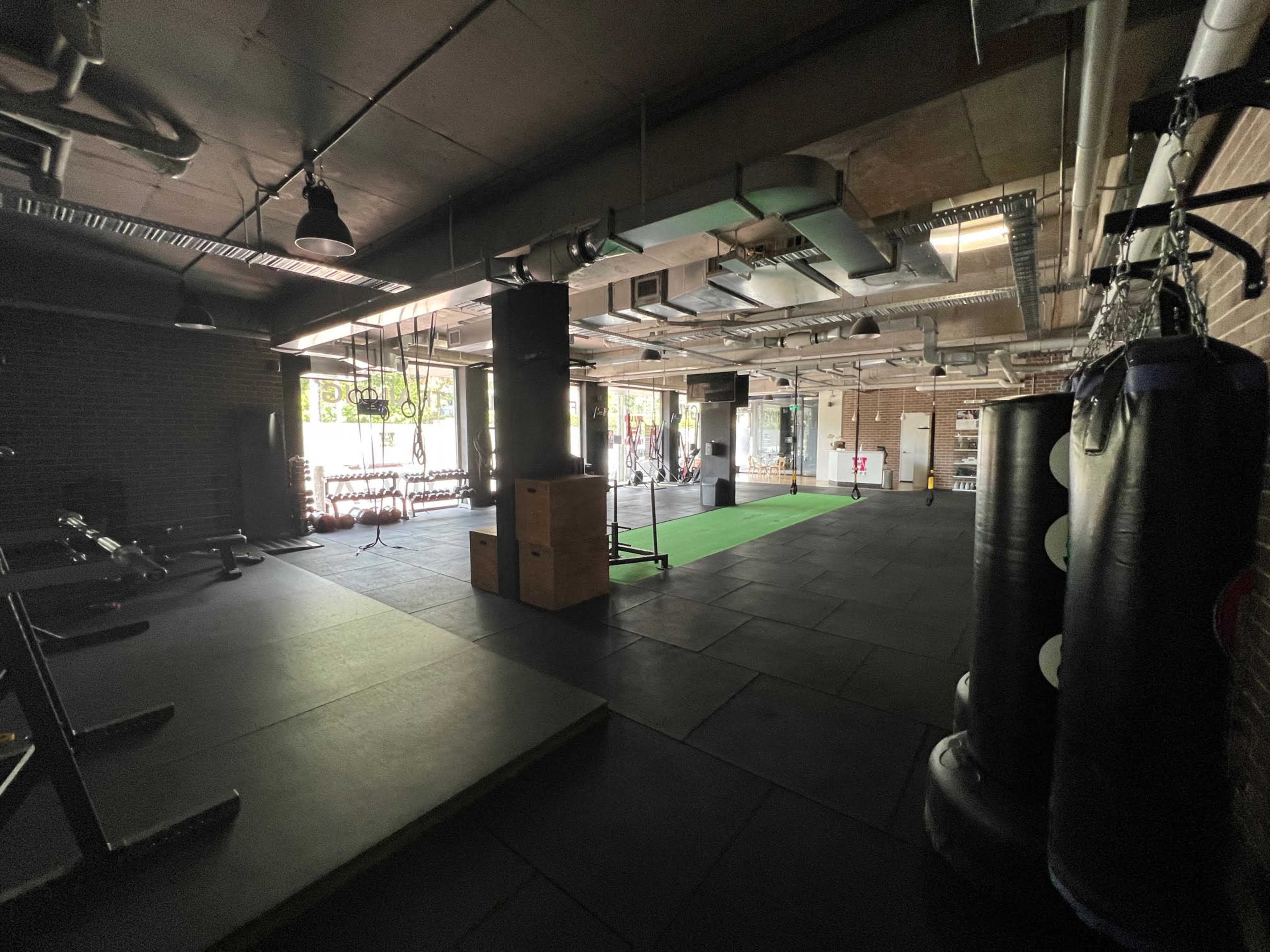 A spacious gym with exercise equipment, including punching bags and fitness mats, under industrial-style lighting.