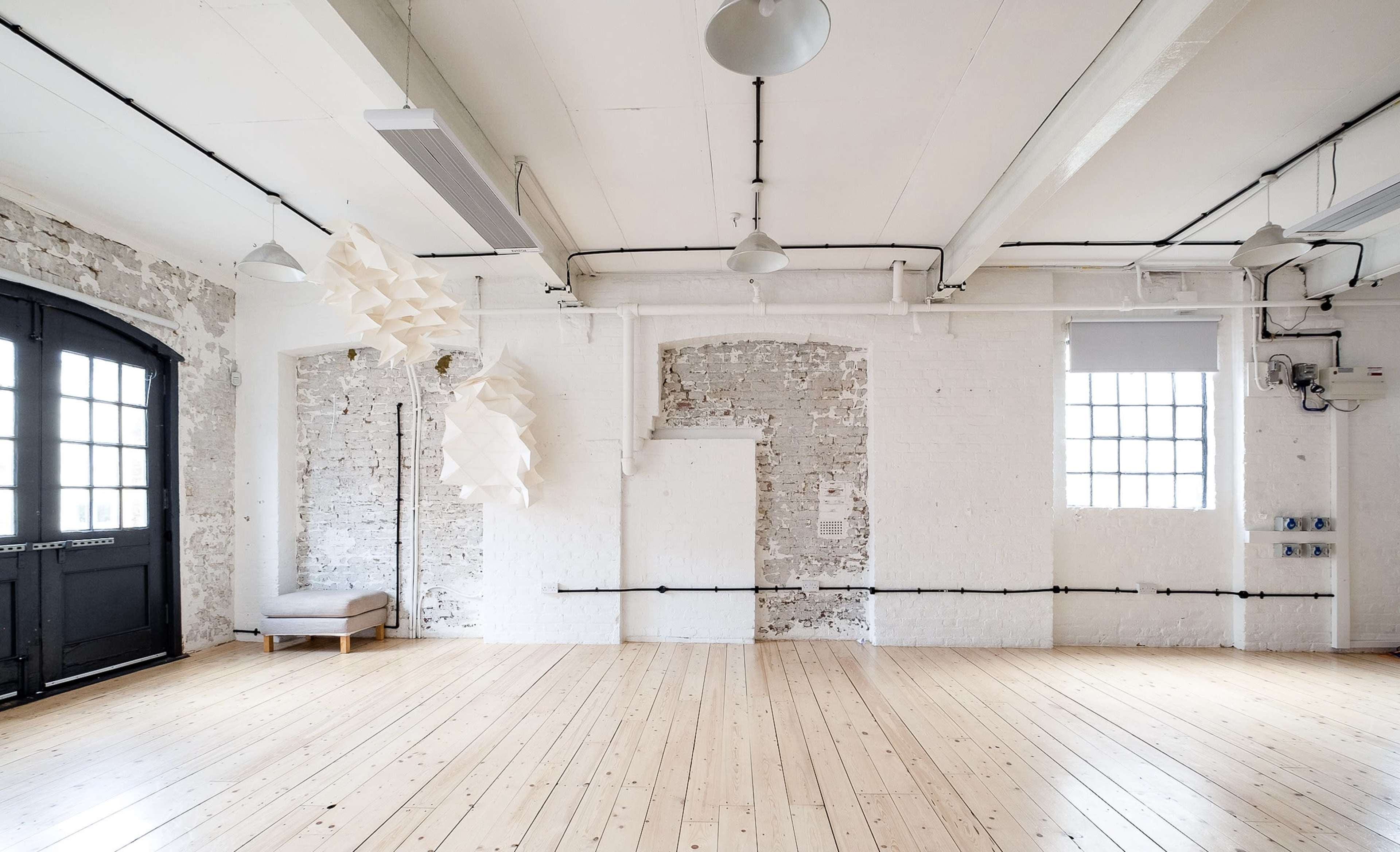 A bright, minimalist interior of a room with exposed brick walls, wooden flooring, and a modern light fixture hanging from the ceiling.