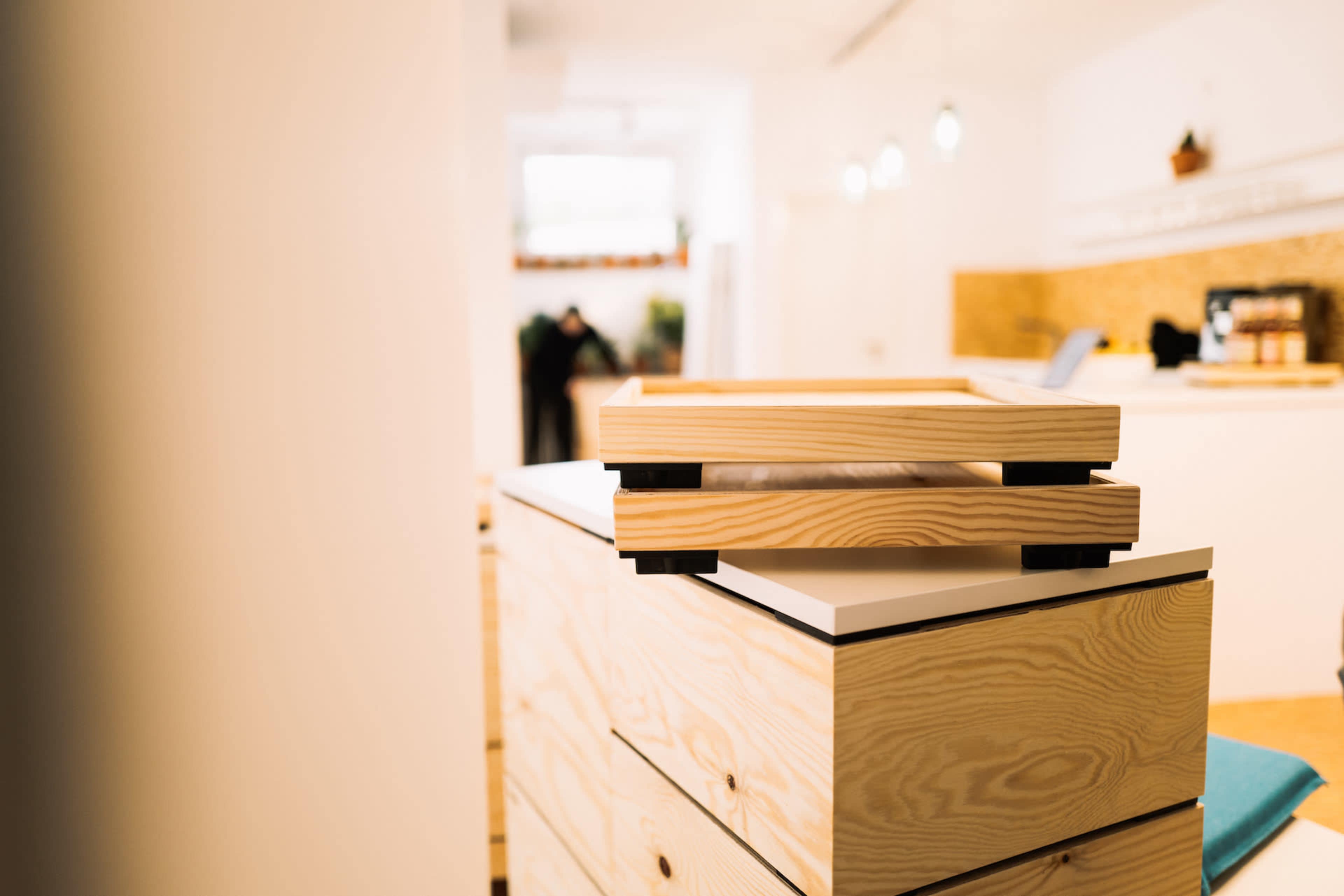 A stack of wooden trays rests atop a modern, minimalist dresser in a brightly lit interior space.