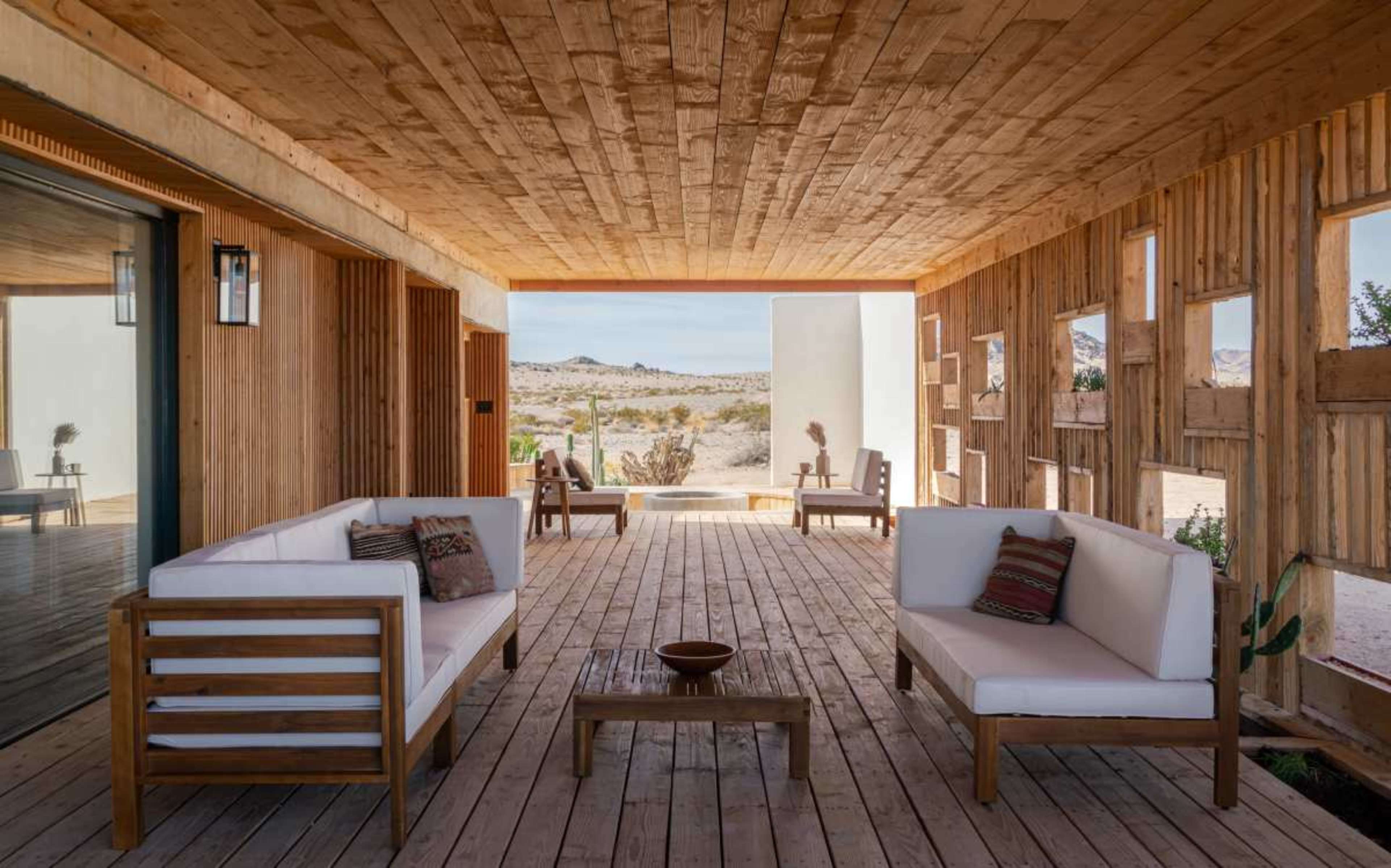 The image shows a wooden porch area with modern seating and a view of a desert landscape in the background.