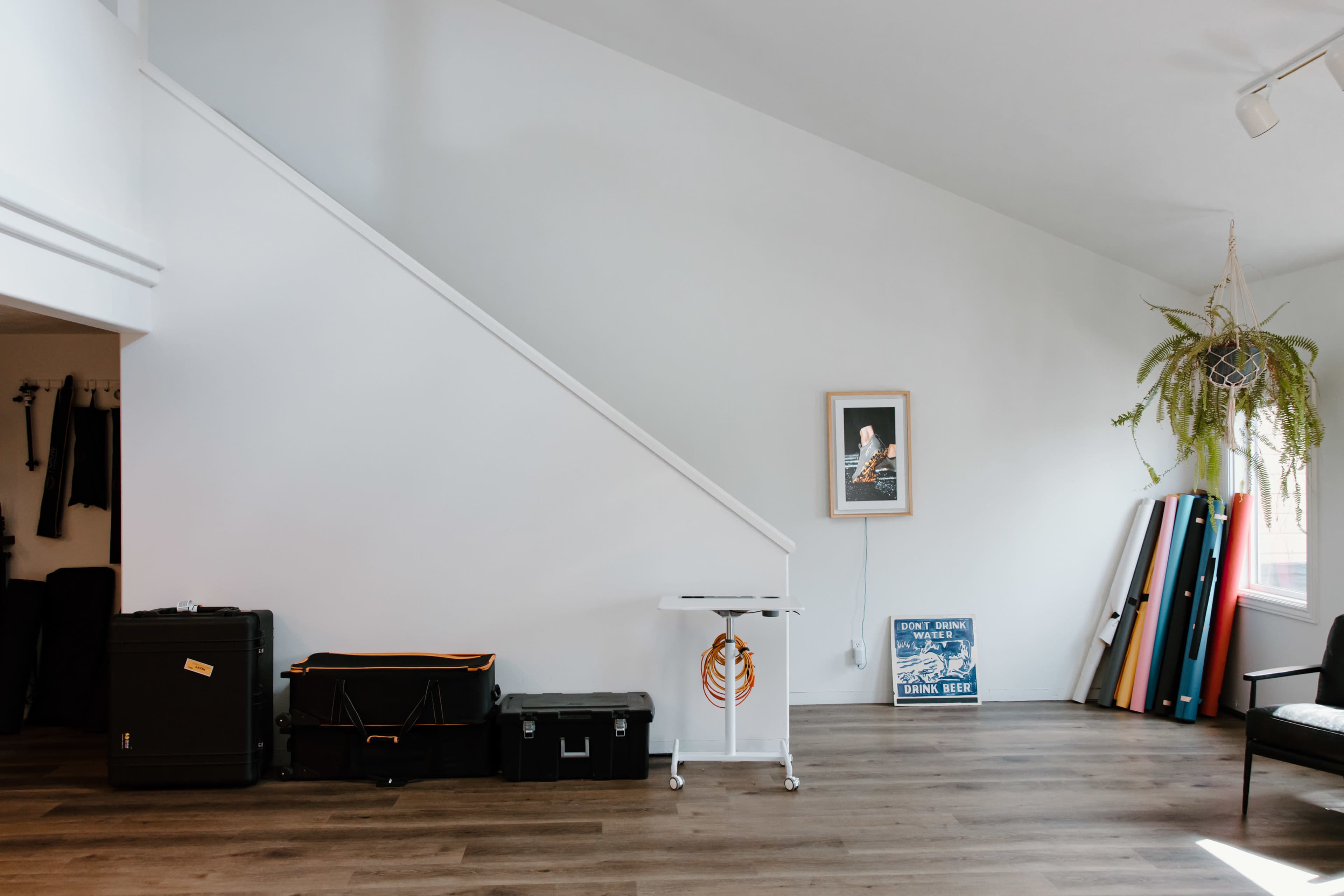 A modern interior space with a sloped white wall, a small table, various fitness mats, and storage boxes along the floor.