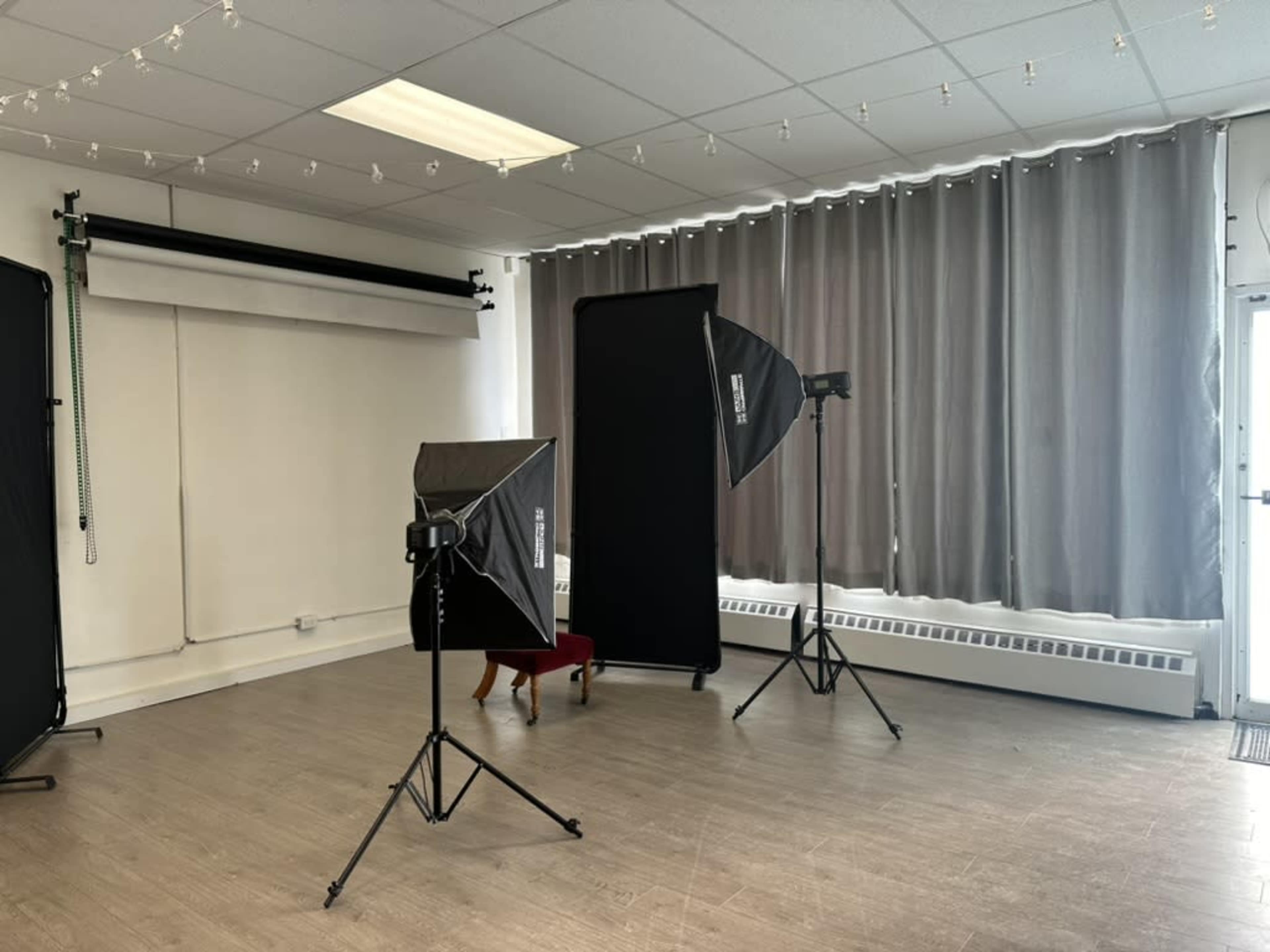 A photography studio with two softboxes, a backdrop holder, and large curtains covering a window.