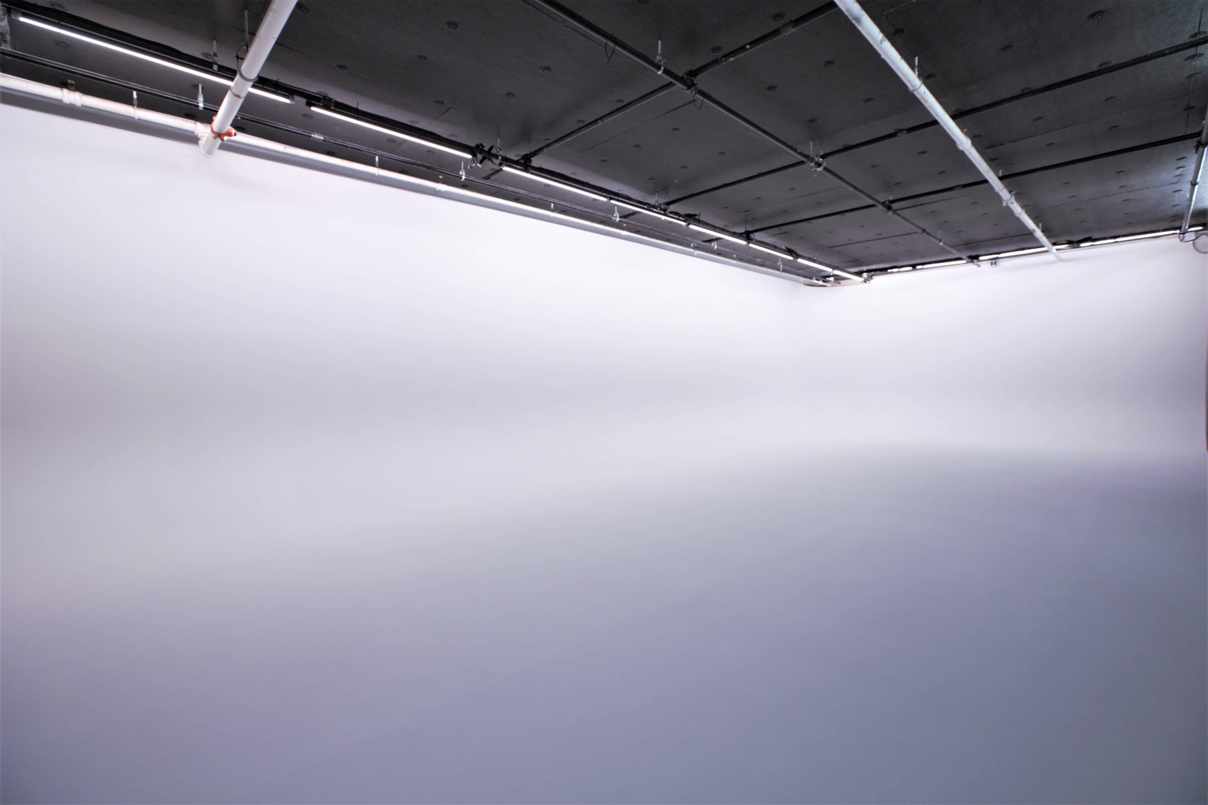 The image shows an empty studio space with a seamless white background and overhead lighting.