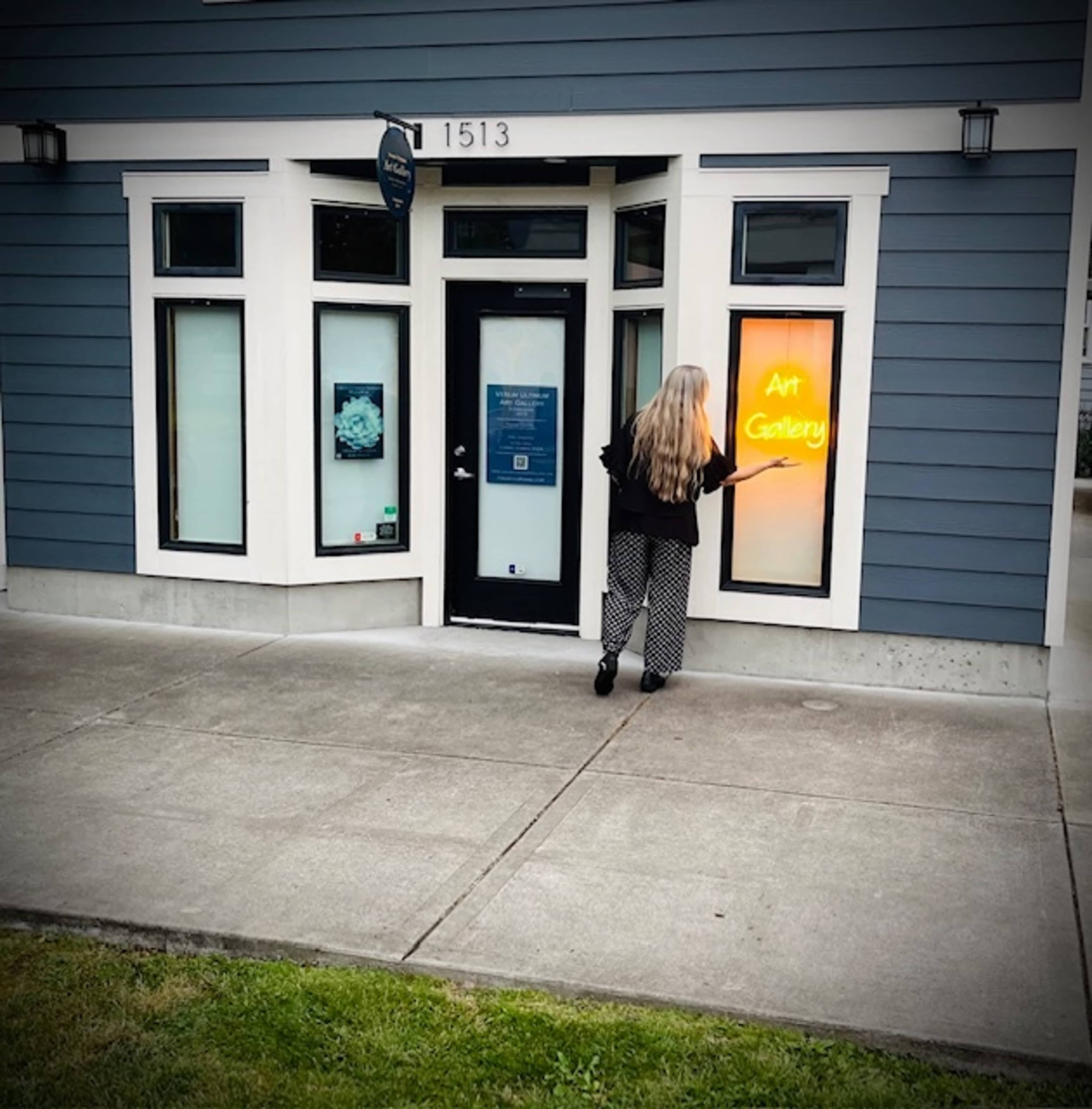 A woman with long hair stands outside an art gallery, interacting with a neon "Art Gallery" sign in the window.
