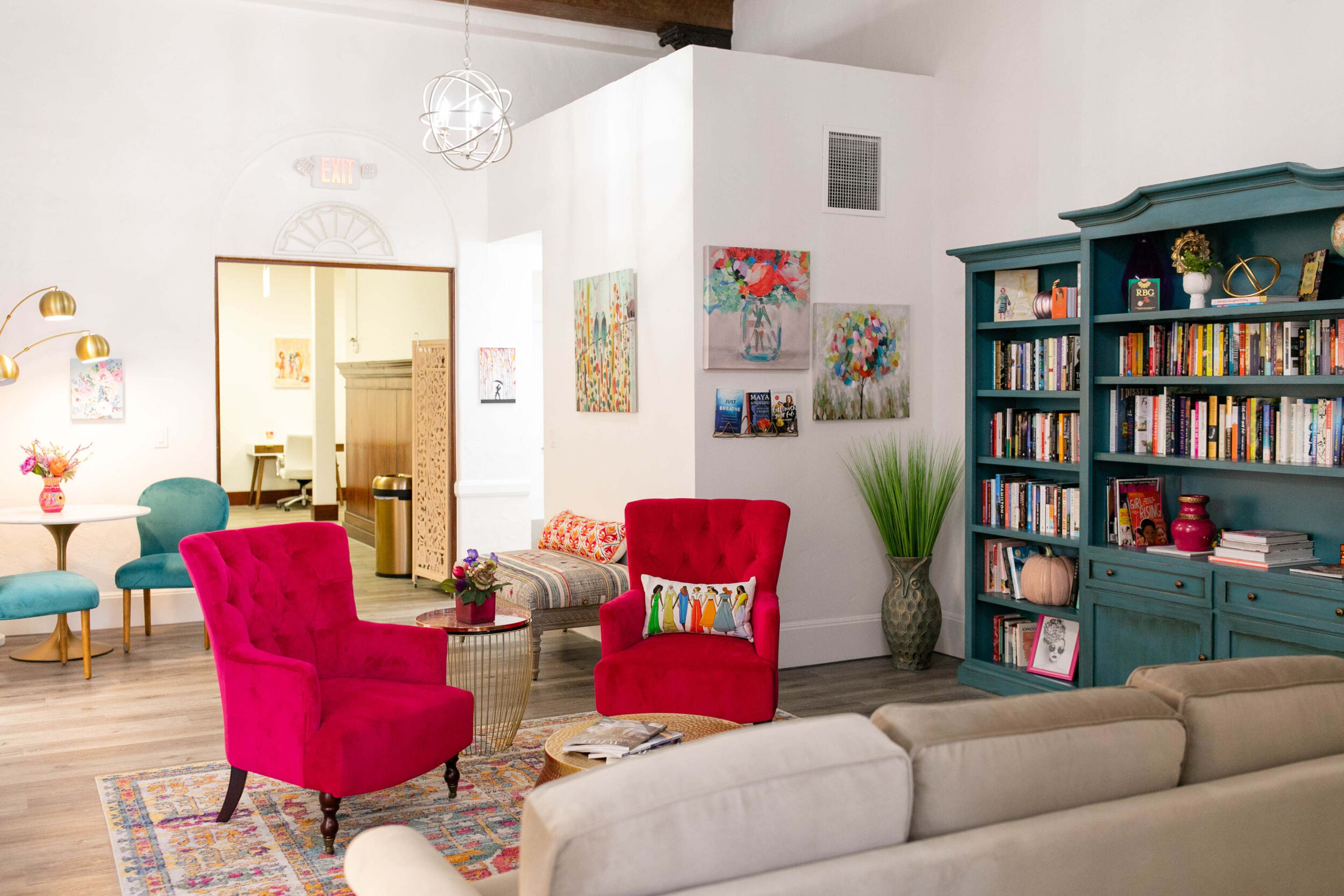 A bright and airy living space featuring colorful furniture, a bookshelf filled with books, and vibrant artwork on the walls.