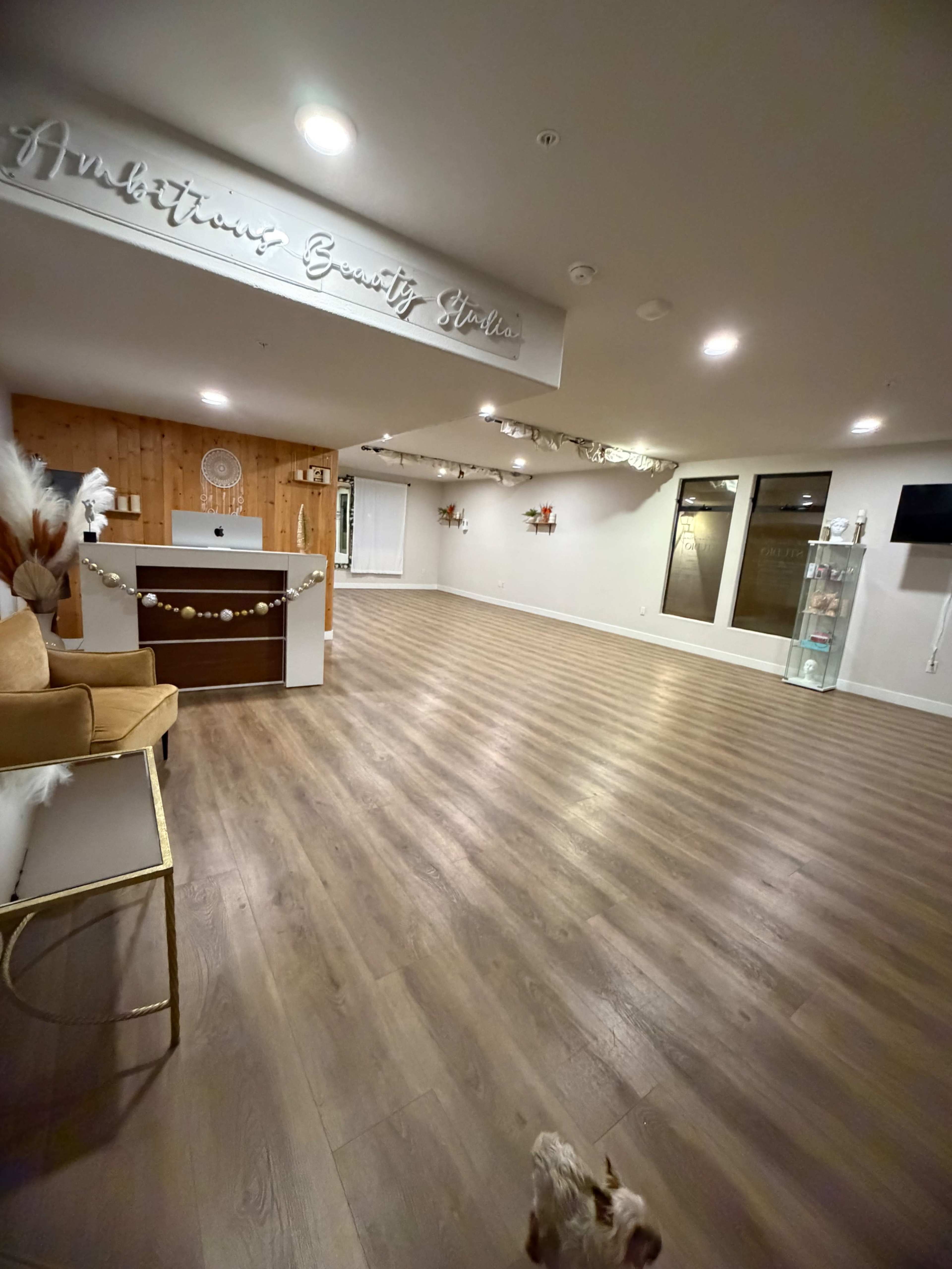 The image shows a spacious, well-lit interior of a beauty salon with wooden flooring, a reception desk, and minimal decor.