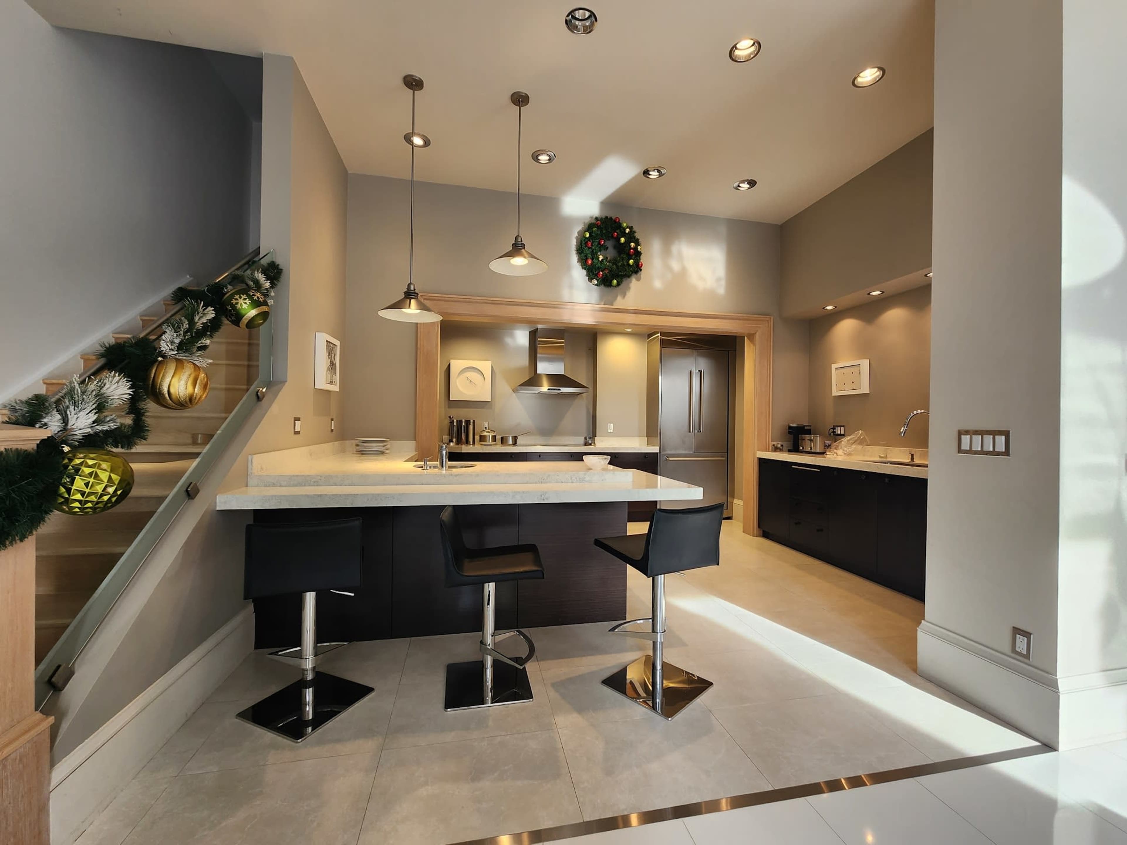 A modern kitchen with a central island, bar stools, and festive decorations on the staircase.
